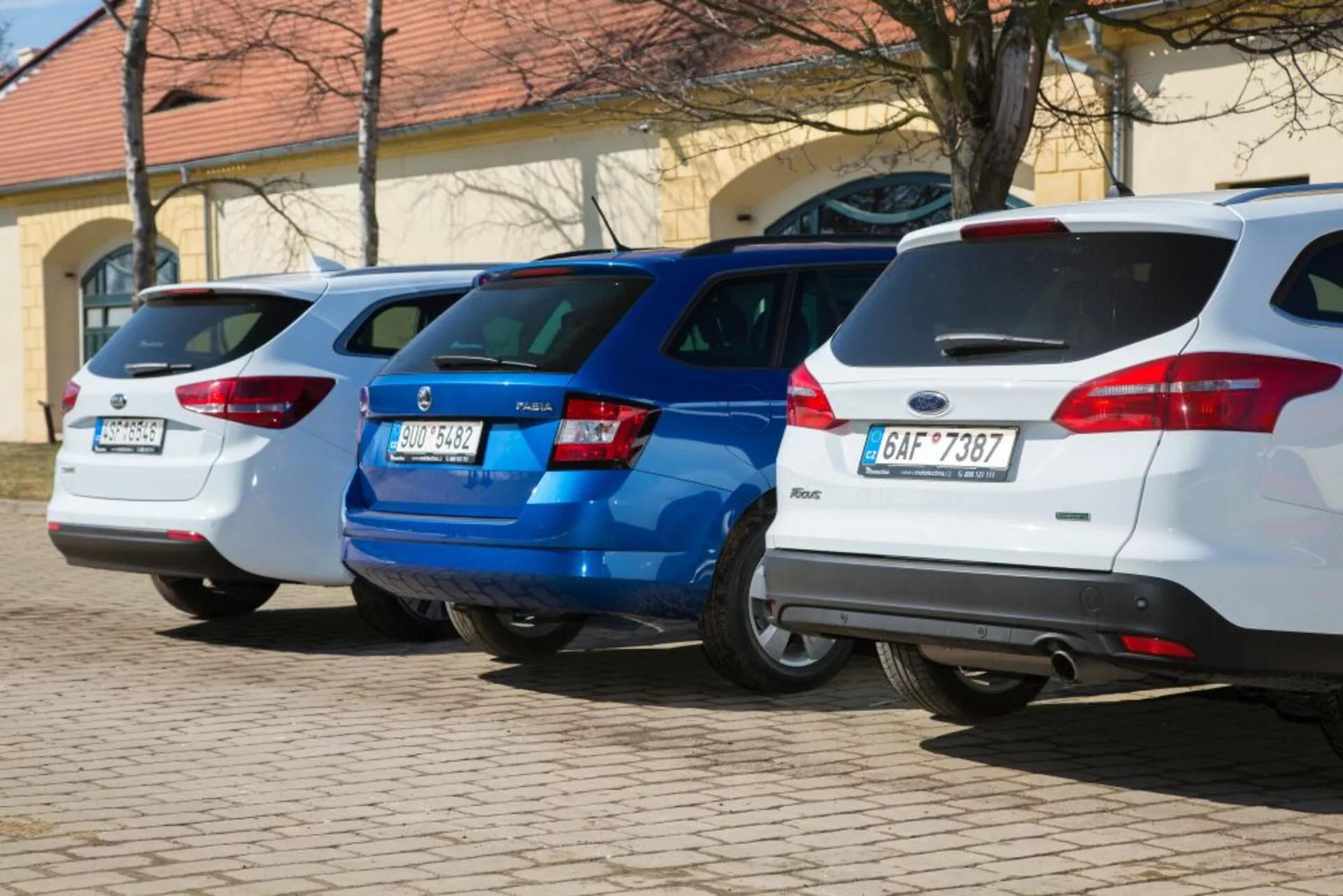 Linia trzech hatchbacków, w tym biały Ford Focus z 2011 roku, zaparkowanych prostopadle tyłem do kamery, prezentująca tylne światła i cechy konstrukcyjne tylnej części na dobrze oświetlonym parkingu.