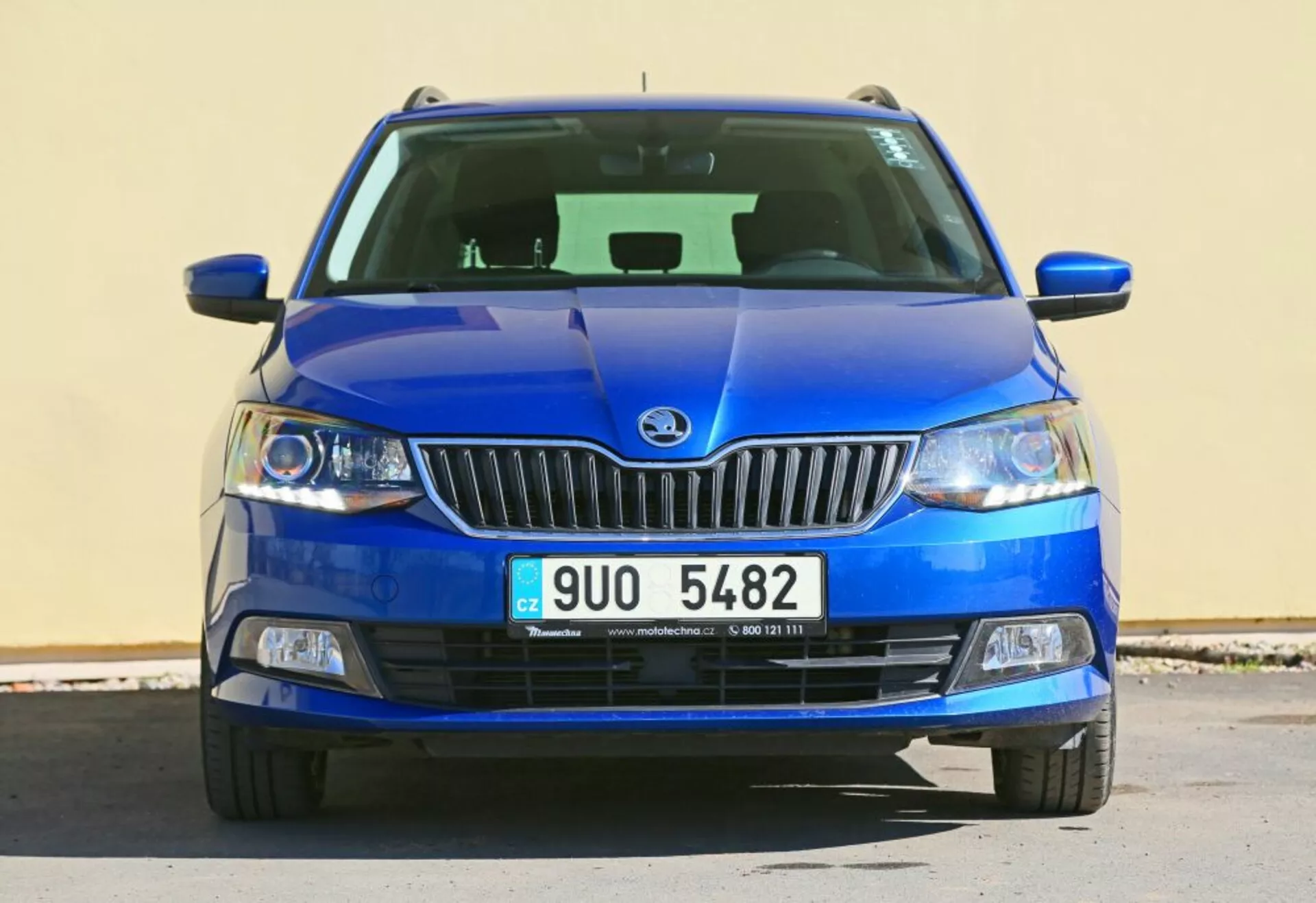 Czołowy widok niebieskiego pojazdu marki Škoda z emblematem marki na chromowanej grillu, światła przednie z przezroczystymi soczewkami i światła przeciwmgielne w czarnej obudowie, z detalicznie opracowaną dolną kratką i rzeźbionym wzorem maski.