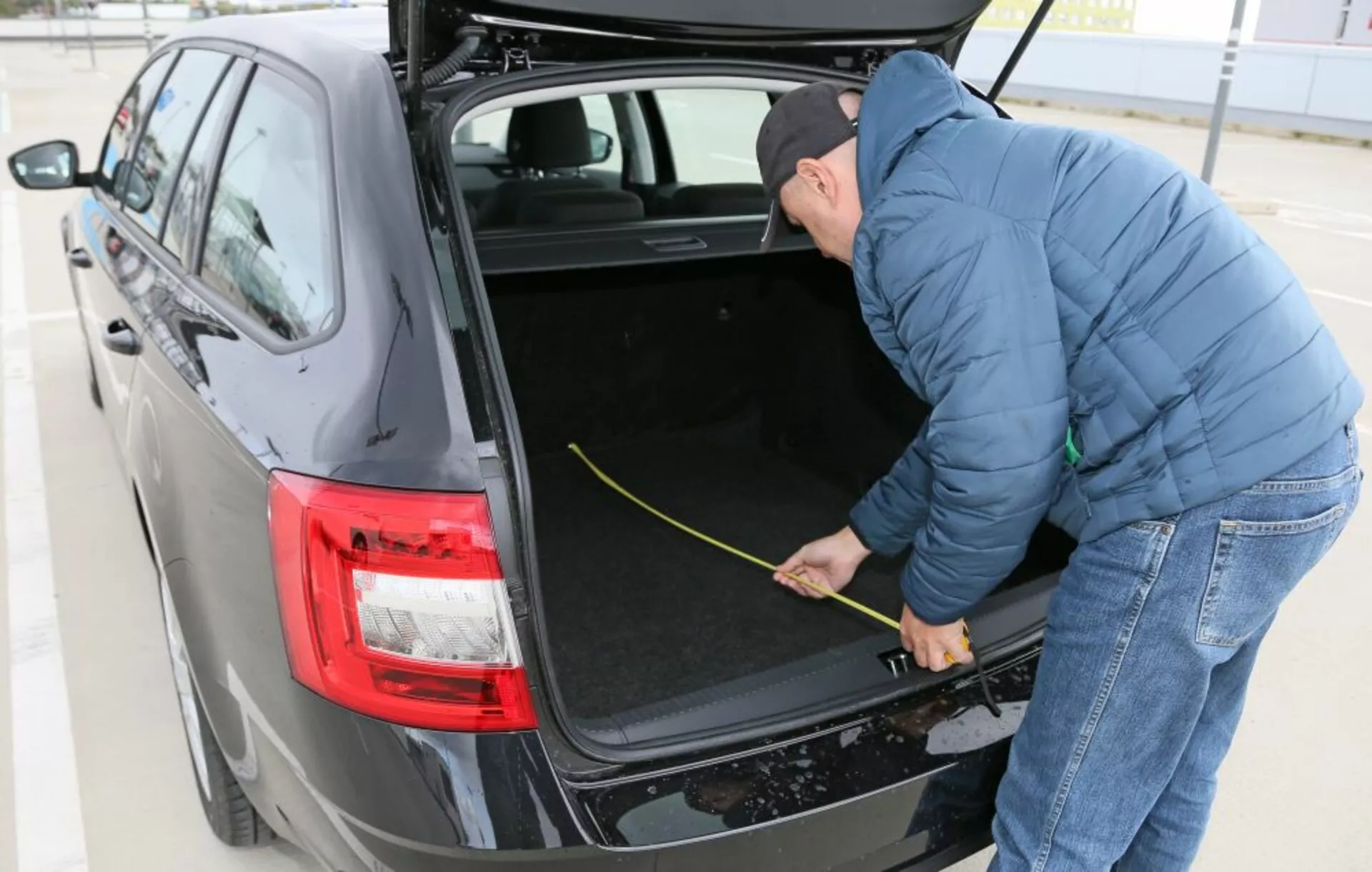 Hyundai i30 2017 (i30-N) prezentujący swój przestronny bagażnik z wnętrzem wyłożonym tkaniną, z nowoczesnymi tylami w technologii LED i osobą mierzącą przestrzeń bagażową, uchwyconą z kąta trzech czwartych w świetle dziennym na zewnątrz
