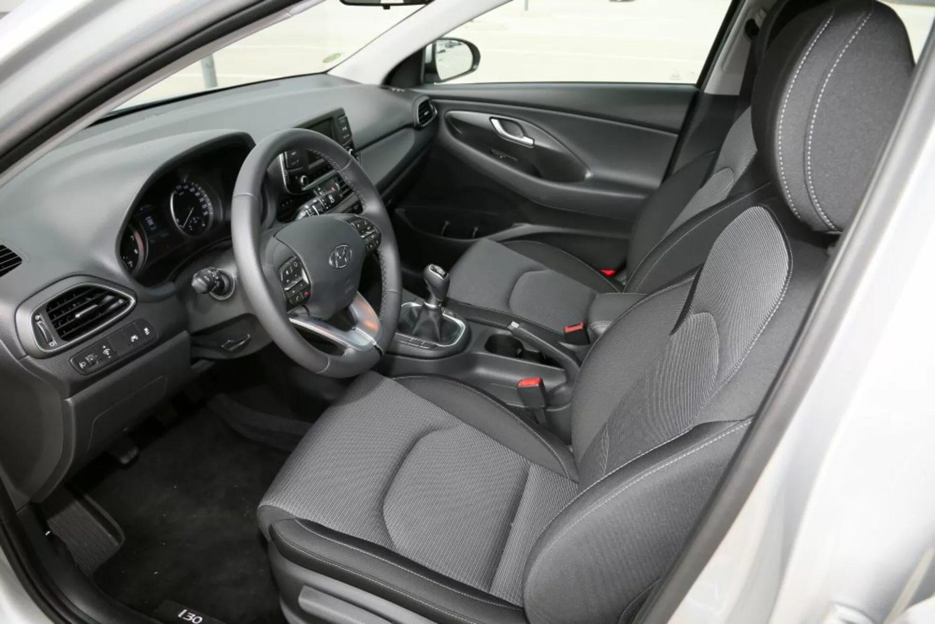 Wnętrze Hyundai i30 2017 (i30-N) skupiające się na przedniej kabinie, pokazujące fotel kierowcy z kontrolami na kierownicy, manualną skrzynią biegów, konsolą centralną i siedzeniami z tkaniny wzorzystej