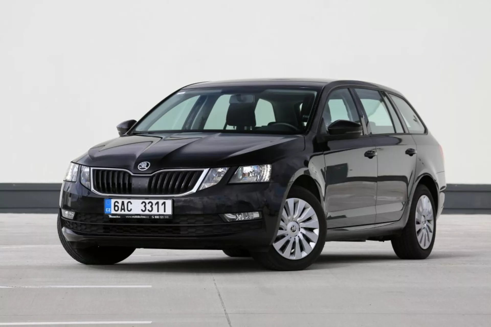 Stacjonarny pojazd marki Škoda widziany z perspektywy frontowej trzech czwartych od strony kierowcy, prezentujący grill, reflektory, maskę, przednią szybę, drzwi kierowcy i tylne drzwi pasażera, część dachu i lewe lusterko boczne na płaskiej powierzchni wewnętrznej z profesjonalnym oświetleniem