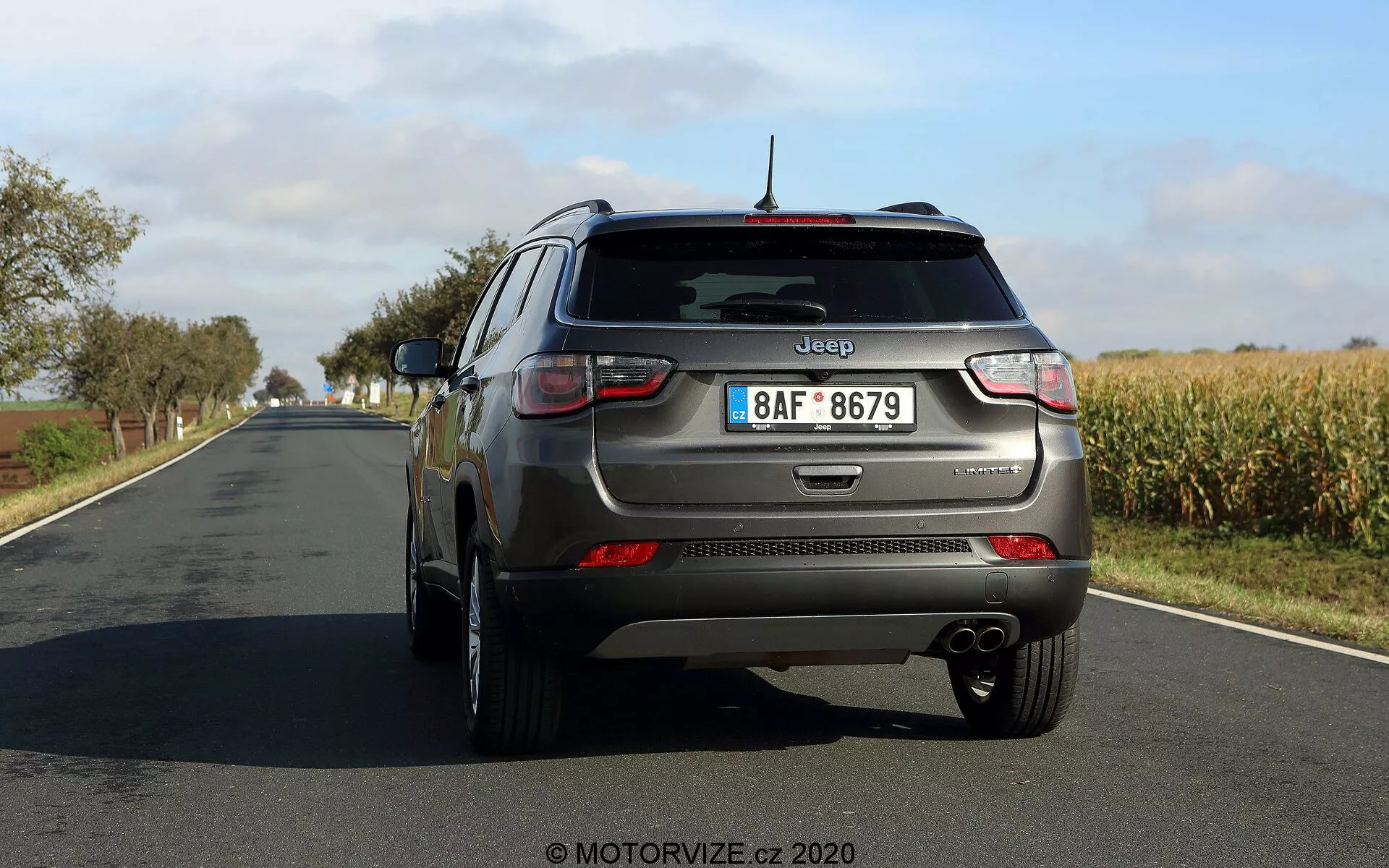Widok trzech czwartych tyłu Jeep Compass 2017 pokazujący charakterystyczne elementy designu, w tym tylne światła, tylny zderzak, podwójny układ wydechowy, oznaczenia marki na klapie bagażnika, wycieraczkę tylnej szyby, pasek odblaskowy, pięcioramienne felgi aluminiowe, antenę montowaną na dachu i odblaski na dolnej krawędzi. Obraz zapewnia wyraźną perspektywę od tyłu i nieco od strony kierowcy z dużą ilością miejsca między samochodem a aparatem.