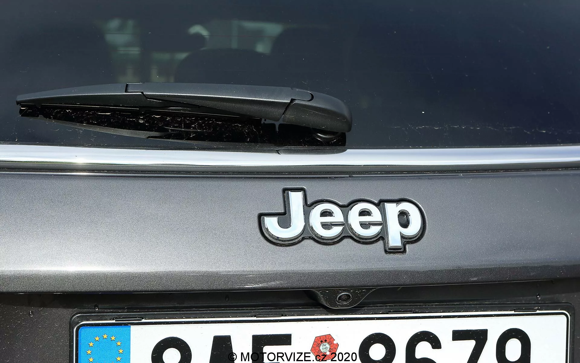 Zbliżenie tylnej części Jeepa Compass 2017 z wyeksponowanym logo Jeep, tylną wycieraczką i częściowo widoczną europejską tablicą rejestracyjną z zamazanym identyfikatorem kraju