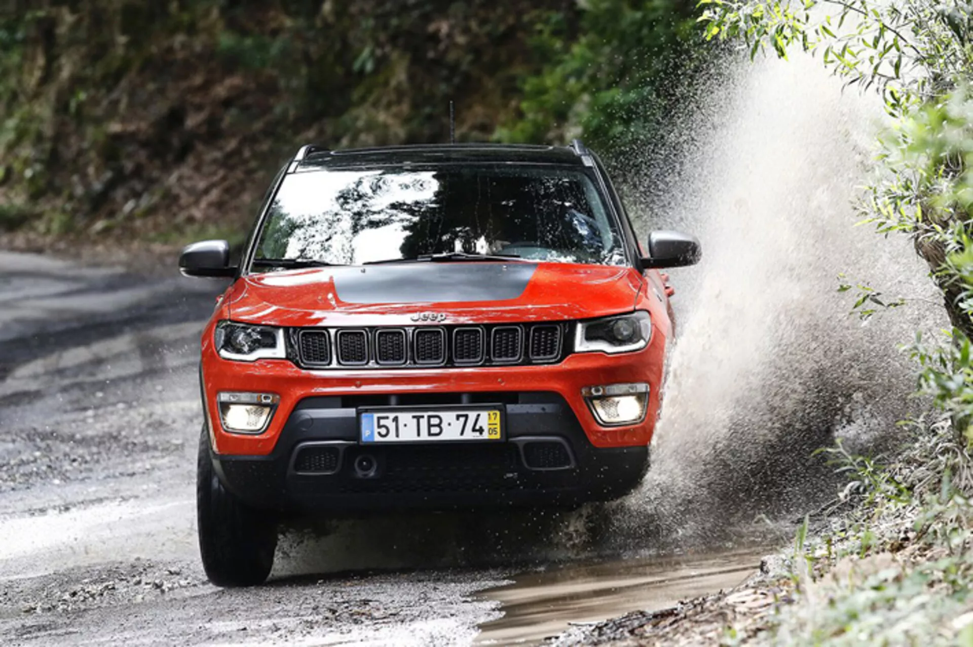 SUV Jeep Compass 2017 w dynamicznej akcji terenowej, pokazany z przedniego trójkwartalnego kąta podkreślającego jego solidną konstrukcję i możliwości jezdne na błotnistej leśnej ścieżce.