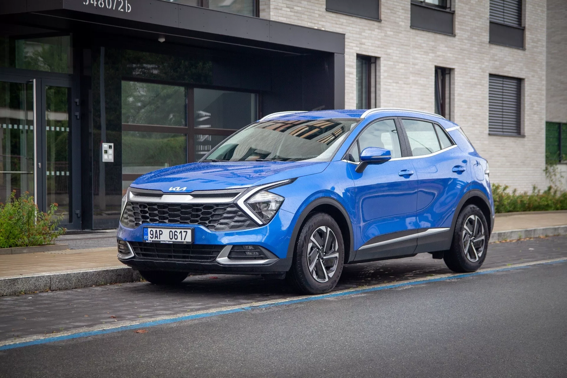 Niebieskie Kia Sportage 2022, z widokiem trzy czwarte z przodu na miejskiej ulicy, podkreślające jego wysoką pozycję, reflektory LED, felgi aluminiowe i nowoczesne technologie bezpieczeństwa.