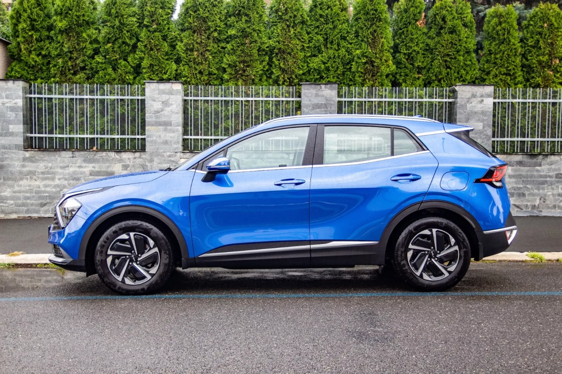 Crossover SUV Kia Sportage 2022 w jaskrawym błękicie, prezentujący swój smukły, kompaktowy projekt z dachem o profilu coupé, profilowaną maską, jednostkami reflektorów LED, pięcioramienne koła ze stopu oraz ulepszenia aerodynamiczne, takie jak tylny spoiler, na przedmieściach.