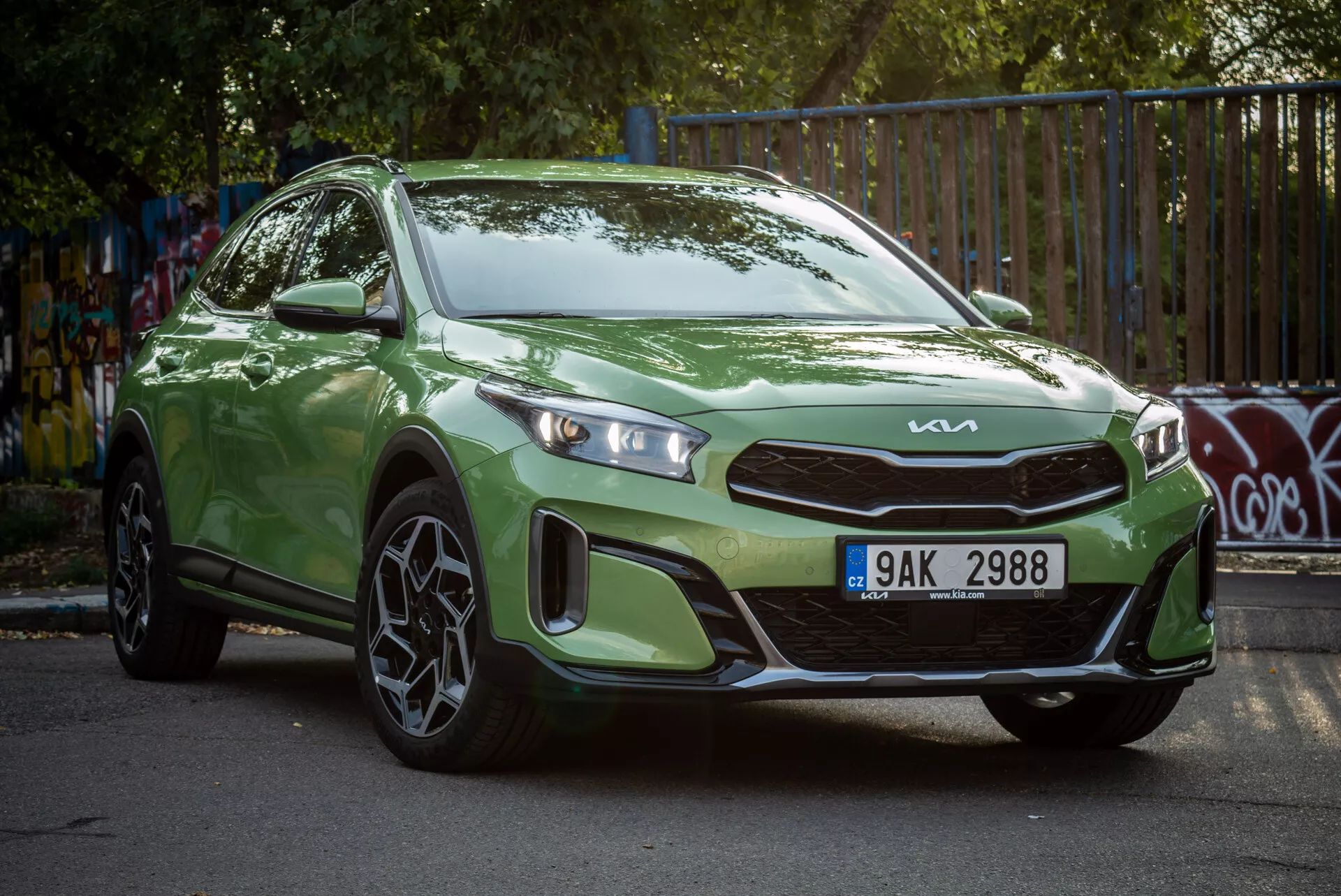Zielony Kia Xceed 2022 zaparkowany pod kątem, prezentujący widok z przodu pod trzema czwartymi z reflektorami LED i sportowymi felgami aluminiowymi w miejskim otoczeniu