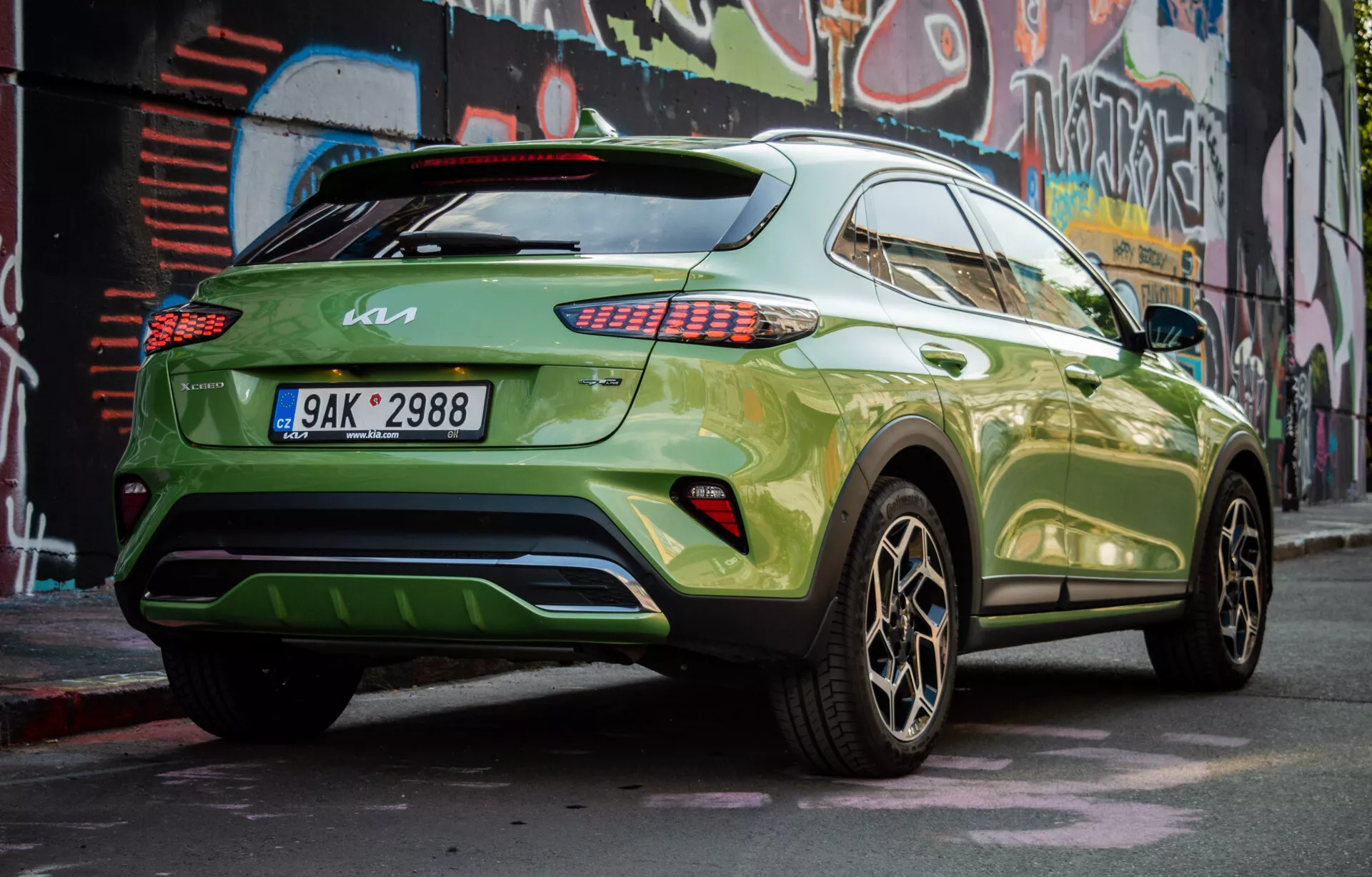 Nowoczesne SUV crossover Kia XCeed 2022 zaparkowane ukośnie, ukazujące jego prawą tylną ćwiartkę, z żywą zieloną farbą i ciemnymi kołami ze stopu, demonstrujące boczny profil pojazdu, tylny design, tylne światła LED, przyciemniane szyby, spoiler dachowy i potencjalny dyfuzor tylny