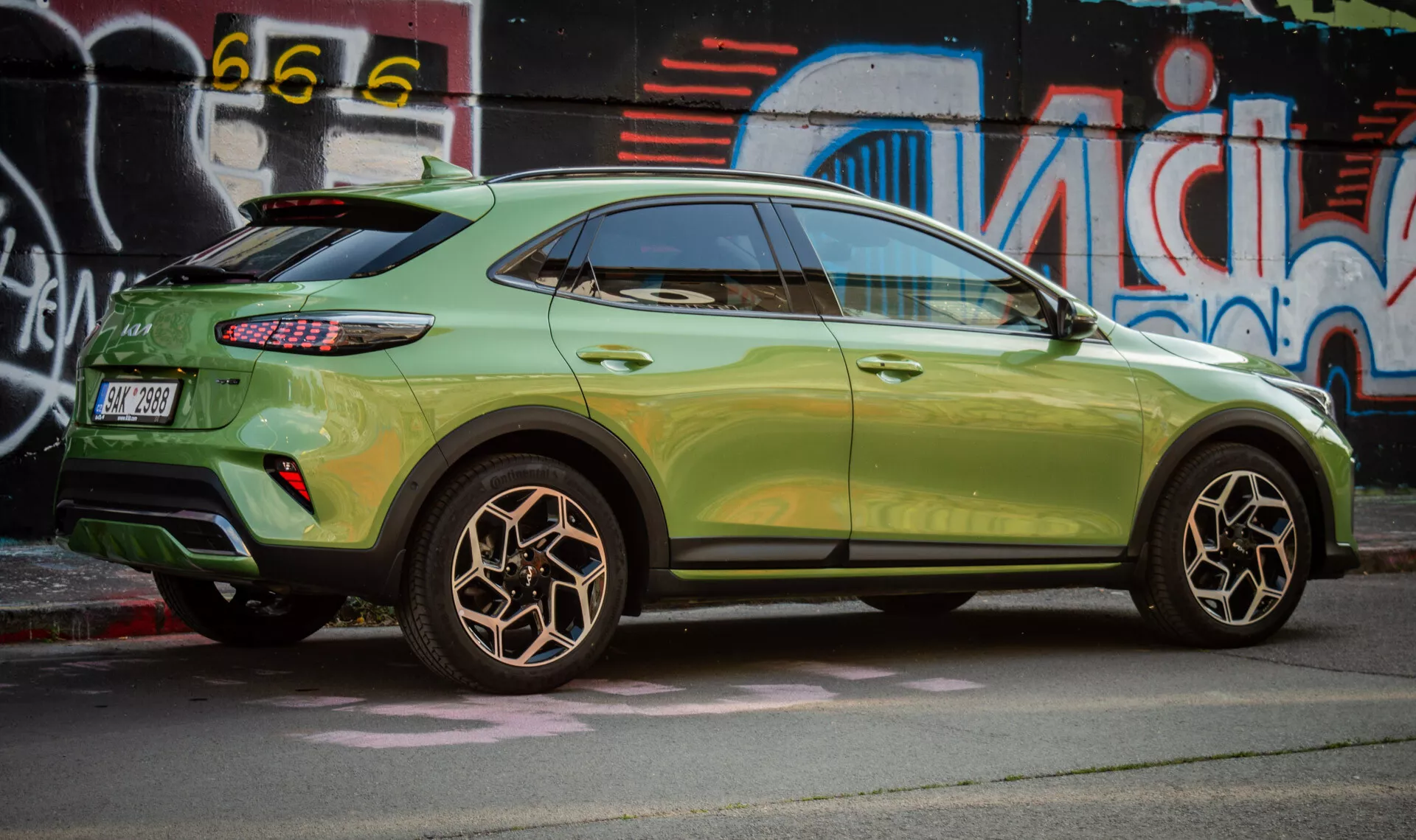 Widok z boku Kia XCeed 2022 podkreślający projekt koła tylnego, metaliczny zielony lakier, tylne światła LED oraz stylizację kompaktowego SUV-a z cechami aerodynamicznymi na tle miejskiej sztuki ulicznej.