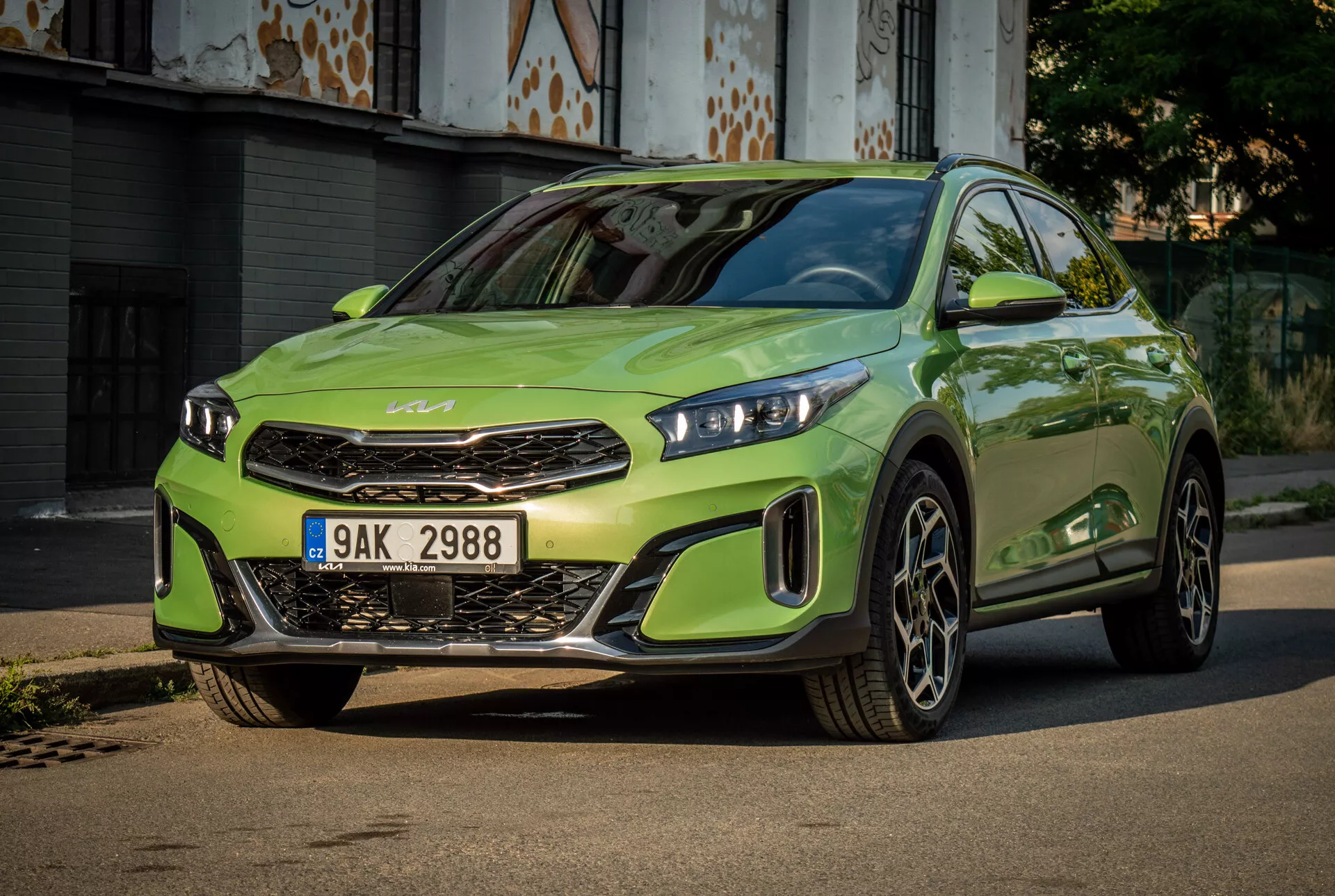 Kia XCeed 2022 w jaskrawej limonkowej zieleni z LEDowymi reflektorami, wyraźną przednią grillą z emblematem marki, sportowym przednim zderzakiem i dużymi kołami ze stopów lekkich, umieszczona na utwardzonej drodze z miejskim tłem