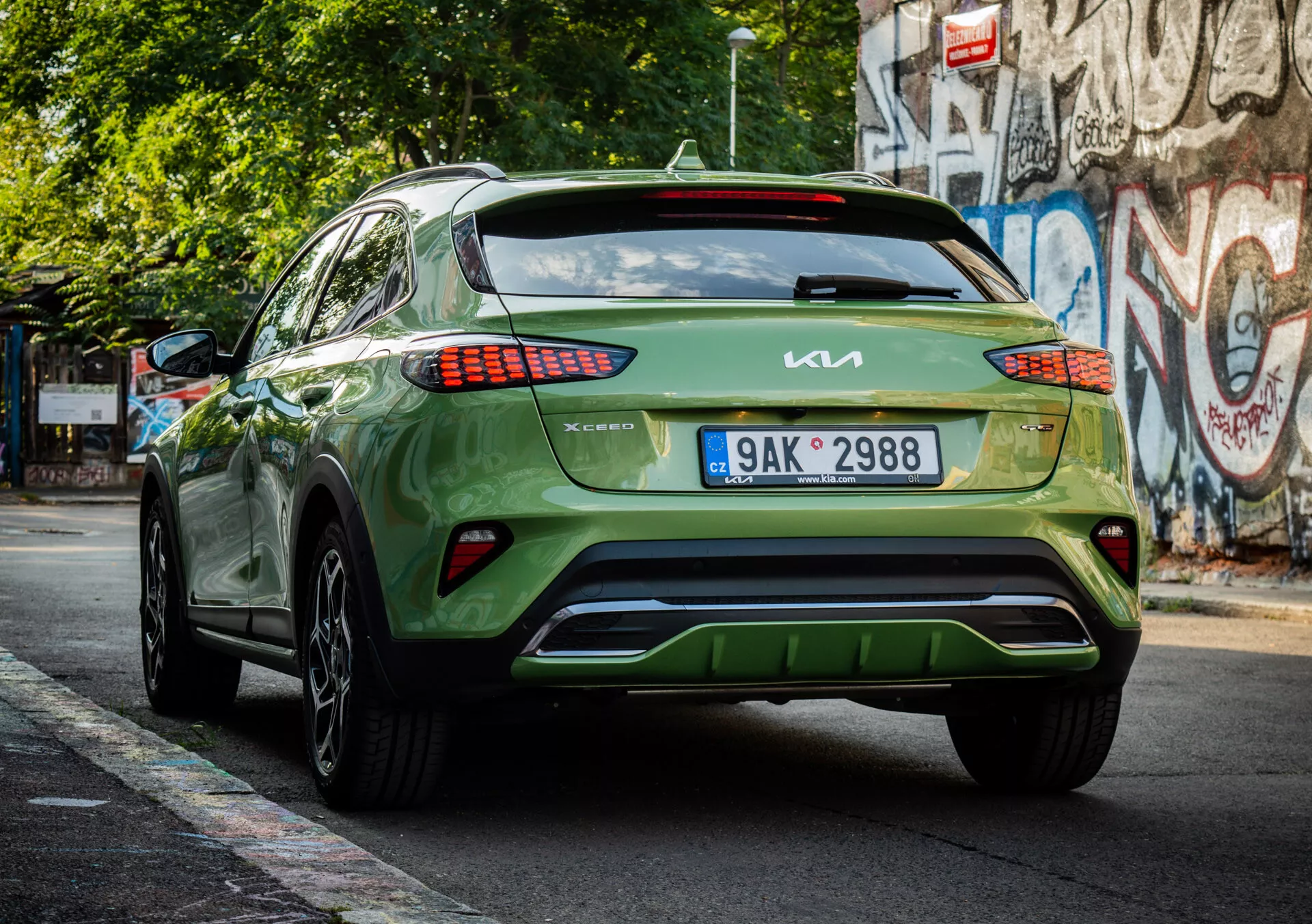 Tylny widok zielonego crossovera/SUV Kia XCeed 2022 ukazujący branding, projekt świateł tylnych LED, umiejscowienie tablicy rejestracyjnej, estetykę dolnego zderzaka oraz błyszczące wykończenie na miejskiej ulicy.