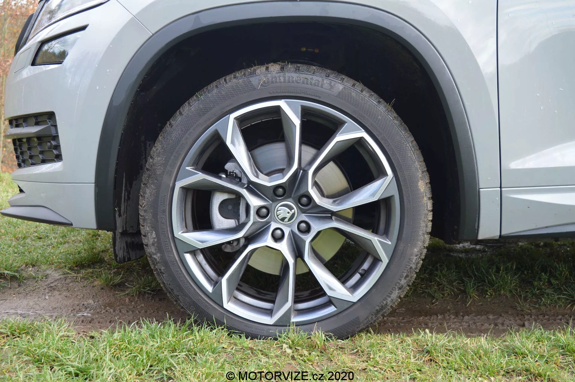 Zbliżenie na przednie koło pasażera w Skodzie Kodiaq z 2017 roku, ukazujące nowoczesny design obręczy ze stopu wieloramiennego, z wykończeniami malowanymi i obrabianymi mechanicznie. Obręcz ma dziesięć szprych o kontrastowych kolorach: ciemnoszarym i jasnym metalicznym, zaprojektowana zarówno dla estetyki, jak i ochrony przed krawężnikiem. Zdjęcie podkreśla także całoroczną lub terenową oponę o widocznym bieżniku i designie z ochroną felgi oraz częściowo przedstawia jasnometalizowany kolor karoserii oraz plastikowy element wykończeniowy wokół nadkola, sugerujący wytrzymały, terenowy charakter SUV-a.