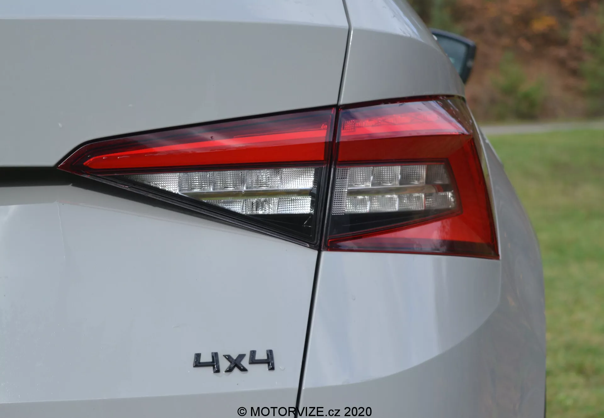 Zbliżenie tylnego fragmentu Skoda Kodiaq 2017, podkreślające współczesny zestaw świateł LED i znaczek '4x4'. Ujęcie pod kątem ukazuje skomplikowane warstwy elementów oświetleniowych, kanciasty design i część tylnego panelu w kolorze srebrnym lub jasnoszarym. Zdjęcie wykonane w ciągu dnia przy naturalnym oświetleniu.