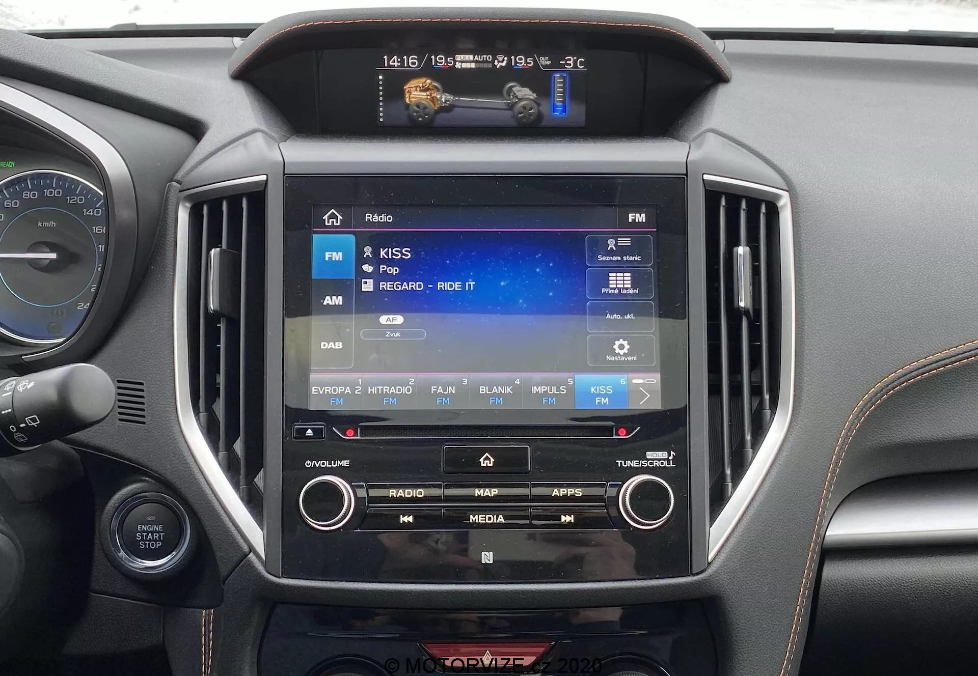 Zbliżenie wnętrza Subaru XV 2018 (Subaru-XV-1-6i-Trend-Lineartronic) skupiające się na centralnym systemie rozrywki. Ekran dotykowy o wielkości około 8-10 cali wyświetla interfejs radia z wybraną opcją FM. Otaczające elementy obejmują fizyczne przyciski i pokrętła do ręcznego sterowania, mniejszy wyświetlacz powyżej wskazujący -3°C, 14:16 i 19/05 oraz symetryczne otwory wentylacyjne. Materiał wokół systemu ma czarne lub ciemnoszare metaliczne wykończenie, typowe dla nowoczesnych wnętrz samochodowych. Widać również część zestawu wskaźników i kierownicy.