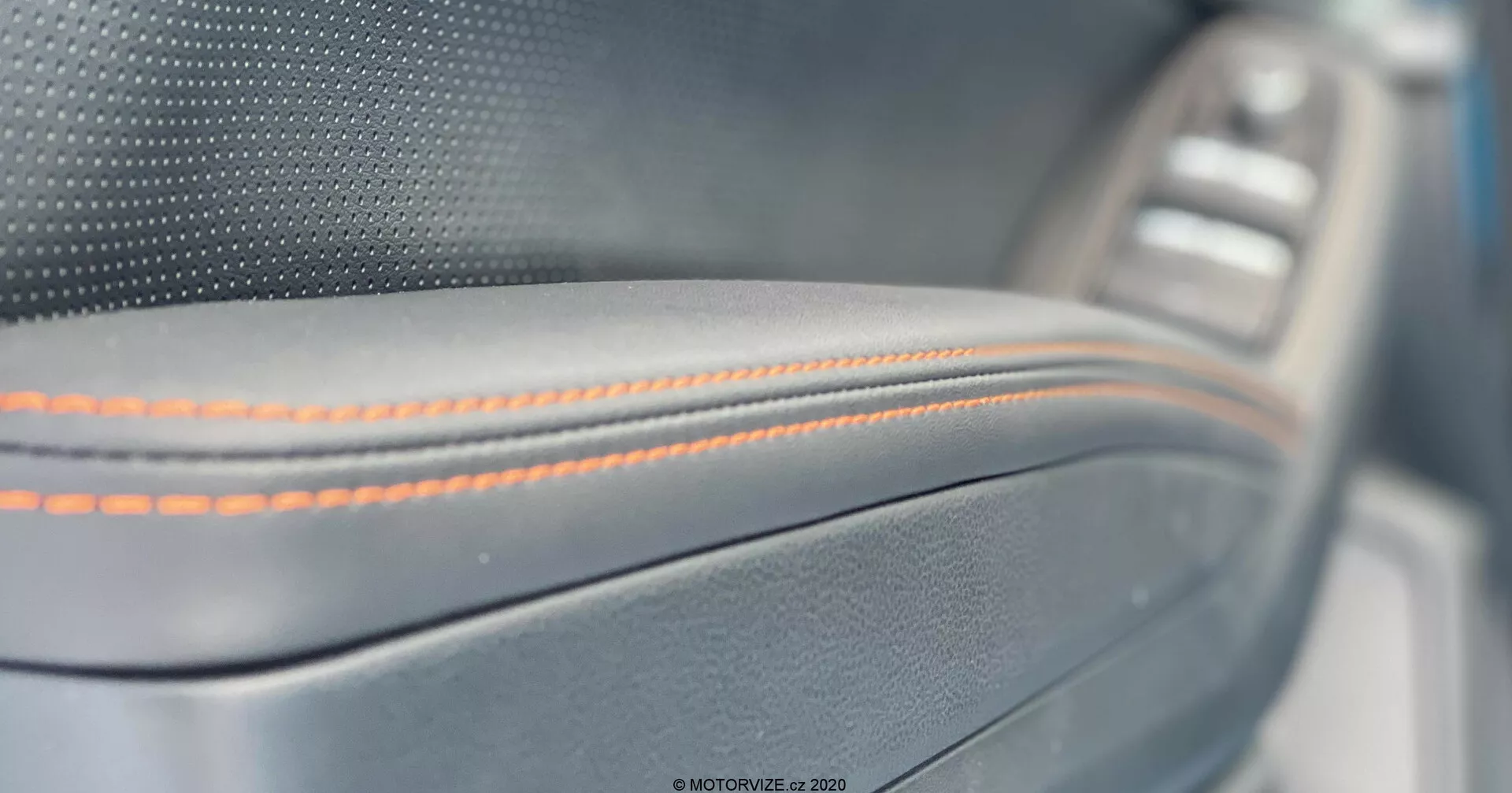 Zbliżenie na wnętrze panelu drzwi Subaru XV 2018, z precyzyjnym pomarańczowym szwem na skórzanym materiale z metalowym wykończeniem i lekko rozmazanym panelem sterowania oknem w tle, ukazującym precyzyjne rzemiosło i luksusowe szczegóły.