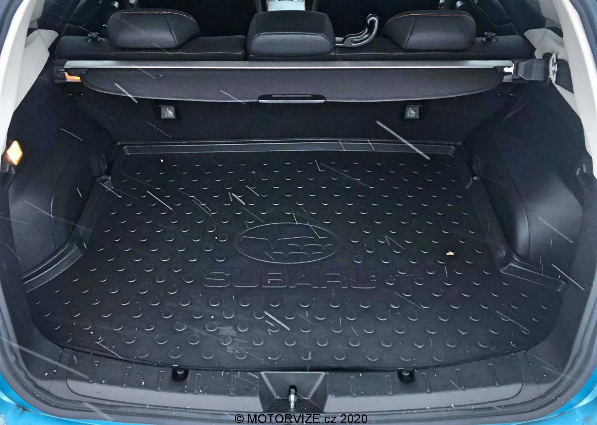 Wnętrze bagażnika Subaru XV 2018 pokazujące przestronną, pustą przestrzeń załadunkową wyłożoną trwałą, wodoodporną matą z logo Subaru, boczne formowane schowki na małe przedmioty, widoczne oparcia tylnych siedzeń z zagłówkami wskazujące, że jest to pojazd 5-osobowy, mechanizm składania tylnej kanapy, punkty kotwiczenia i haki do zabezpieczenia ładunku oraz oświetlenie wewnętrzne dla widoczności.