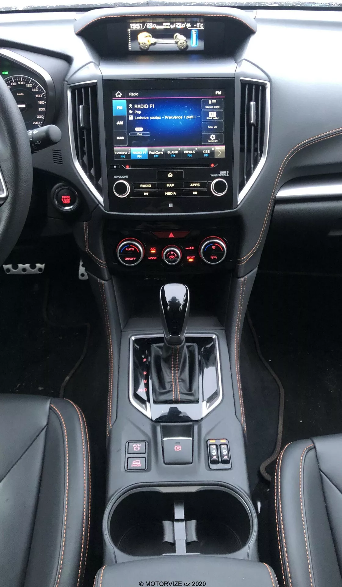 Wnętrze Subaru XV 2018 (subaru-xv-1-6i-trend-lineartronic) pokazujące konsolę środkową i deskę rozdzielczą z perspektywy tylnego siedzenia, z podniesionym systemem infotainment z widocznymi menu, dwustrefową klimatyzacją, ergonomiczną dźwignią zmiany biegów automatycznej, nowoczesnym designem materiałów, uchwytami na napoje i małymi schowkami, różnymi przyciskami sterującymi oraz wielofunkcyjną kierownicą.
