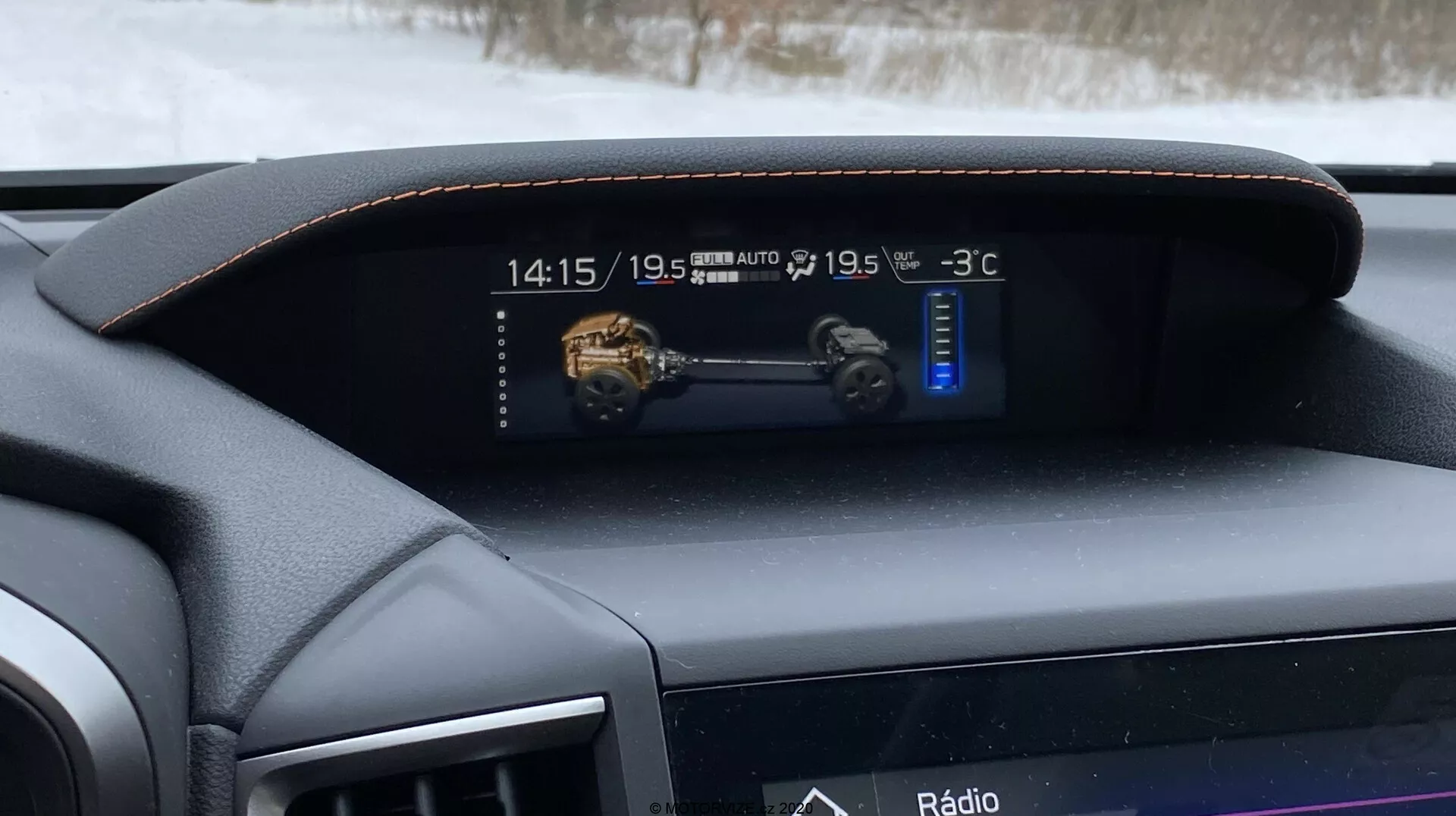 Wnętrze Subaru XV 1.6i Trend Lineartronic z 2018 roku, skupione na cyfrowym zestawie wskaźników i desce rozdzielczej widzianej z fotela kierowcy. Deska rozdzielcza obszyta skórzanym materiałem z ozdobnym przeszyciem podkreśla premium charakter wnętrza. Cyfrowy wyświetlacz pokazuje czas (14:15), model 3D pojazdu, sterowane klimatyzacji dwustrefowej ustawione na 'LO' oraz temperaturę zewnętrzną -3°C. Poniżej, węższy ekran wyświetla aktualną opcję rozrywki 'Radio', co wskazuje na zintegrowany system infotainment.