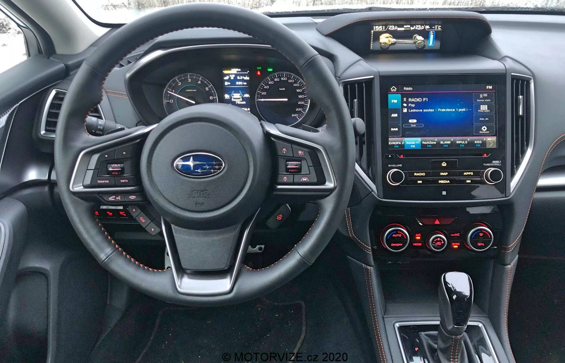 Wnętrze Subaru XV 2018 z perspektywy kierowcy, prezentujące logo Subaru na kierownicy z przyciskami sterującymi, czerwone ściegi, cyfrowy zestaw wskaźników, system multimedialny z ekranem dotykowym w konsoli centralnej, pokrętła sterowania klimatyzacją, porty USB, wejście audio 3,5 mm oraz materiały skórzane (lub podobne) z czerwonymi przeszyciami na desce rozdzielczej i panelach drzwi.