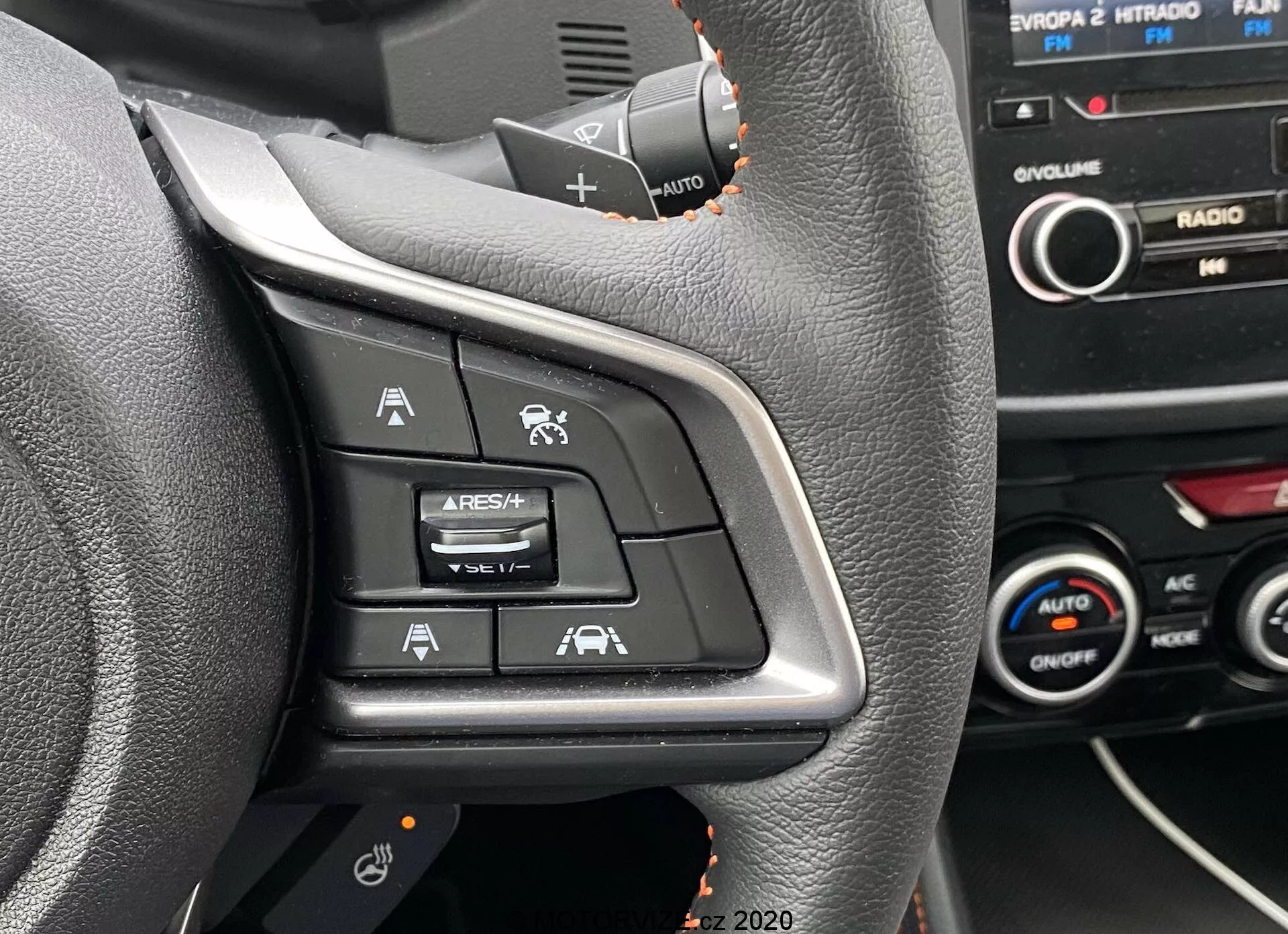 Zbliżenie na lewą stronę panelu sterowania na kierownicy Subaru XV 2018, zawierającym przyciski kontrolujące Adaptacyjny Tempomat, Ogranicznik Prędkości, Komendy Głosowe oraz Asystenta Utrzymania Pasa Ruchu. Zdjęcie wykonane z perspektywy siedzenia kierowcy, podkreślając podświetlone symbole na czarnej plastikowej powierzchni, z widoczną w tle częścią deski rozdzielczej i konsoli środkowej.
