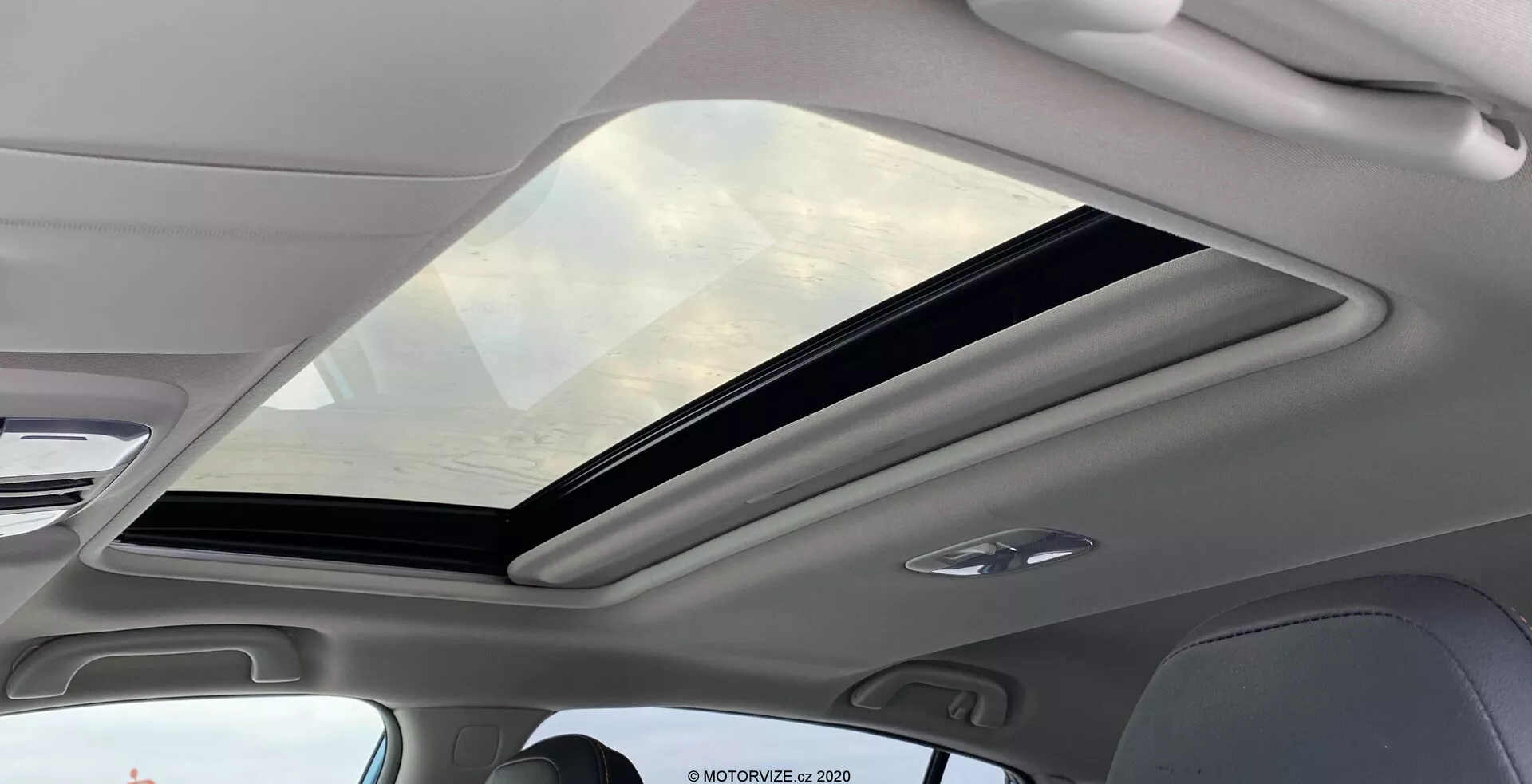 Widok wnętrza Subaru XV 2018 1.6i Trend Lineartronic skupiający się na dużym panoramicznym szyberdachu. Szyberdach rozciąga się od przedniej do tylnej części kabiny, częściowo otwarty z mechanizmem przesuwnym. Szyba przyciemniana oferuje ochronę UV, zwiększając poczucie przestronności wewnątrz. Wnętrze wokół szyberdachu ma jasne wykończenie, które uzupełnia nowoczesną estetykę. Wbudowane lampy LED w podsufitce są widoczne, sygnalizując efektywne energetycznie i długotrwałe oświetlenie.