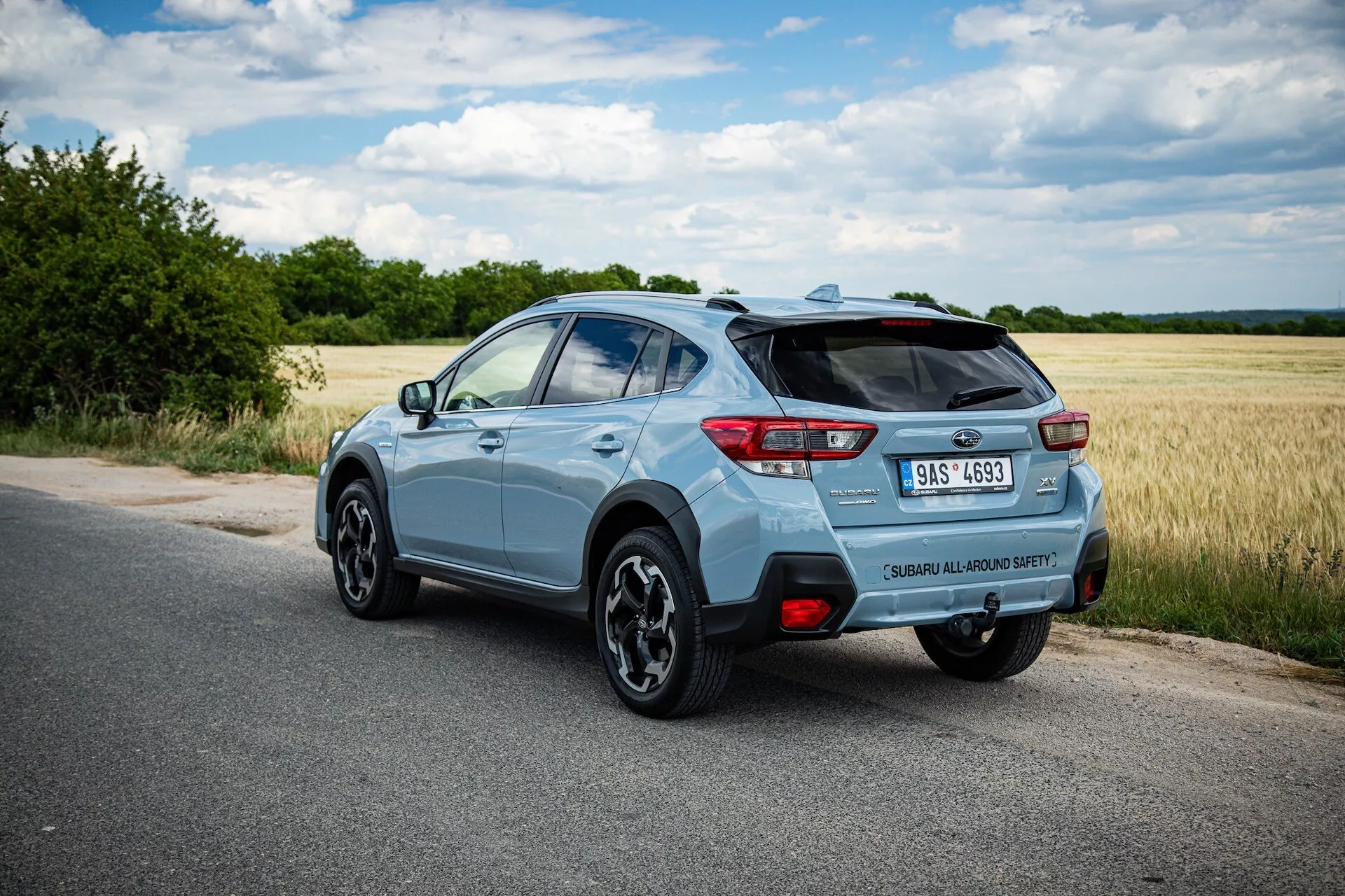 Jasnoniebieski kompaktowy SUV Subaru XV 2021 sfotografowany z tylnego ukośnego kąta podkreślającego prawą stronę, dynamiczną pozycję na utwardzonej drodze z wyraźnym widokiem na tylny spoiler, koła ze stopów, tylne światła LED, oznaczenie modelu, pojedynczą końcówkę wydechu i potencjalne cechy technologiczne