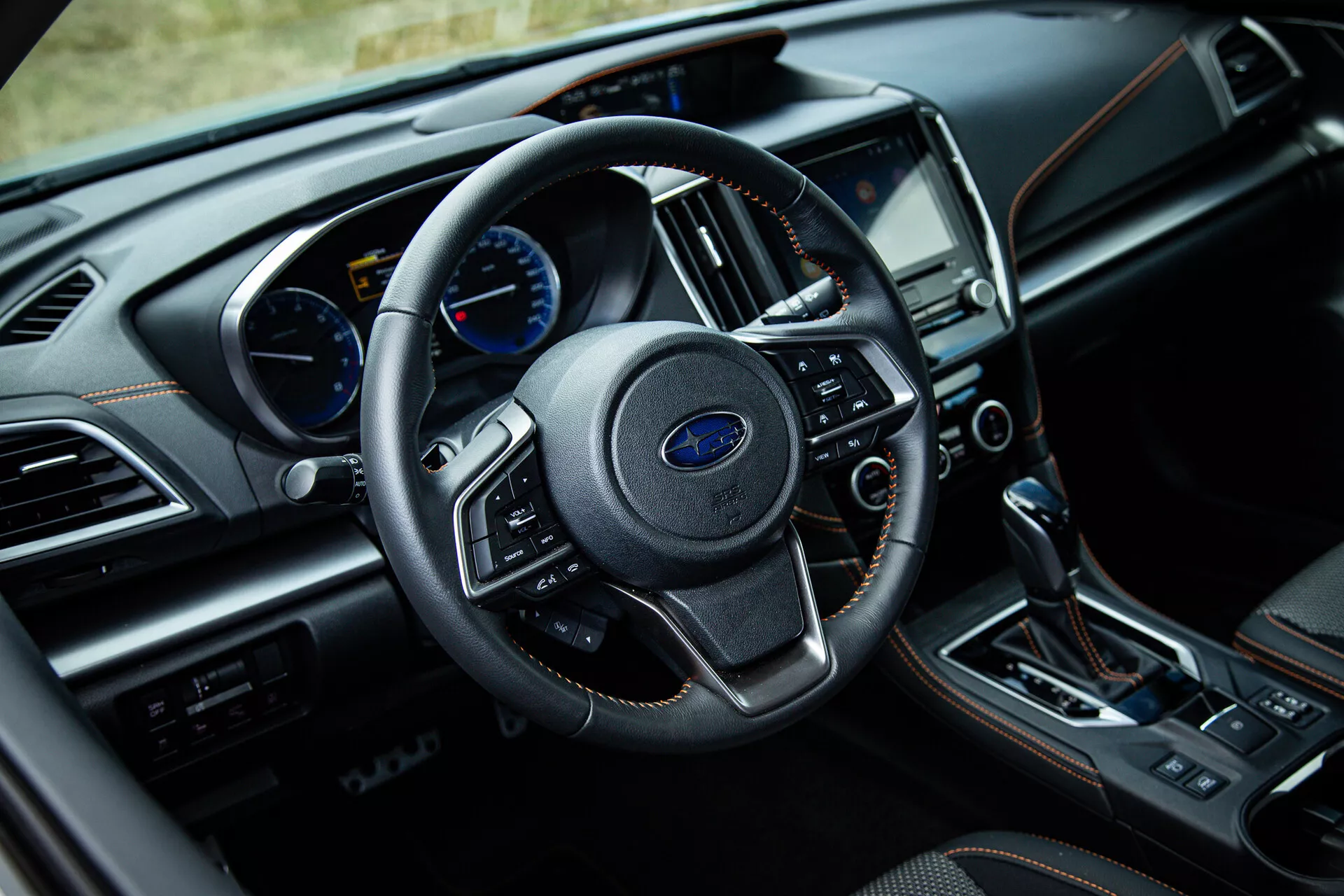 Wnętrze Subaru XV 2021 z perspektywy kierowcy z centralnie umieszczoną skórzaną kierownicą z zamontowanymi przyciskami, analogowo-cyfrowym zestawem wskaźników, ekranem dotykowym systemu infotainment i automatyczną skrzynią biegów