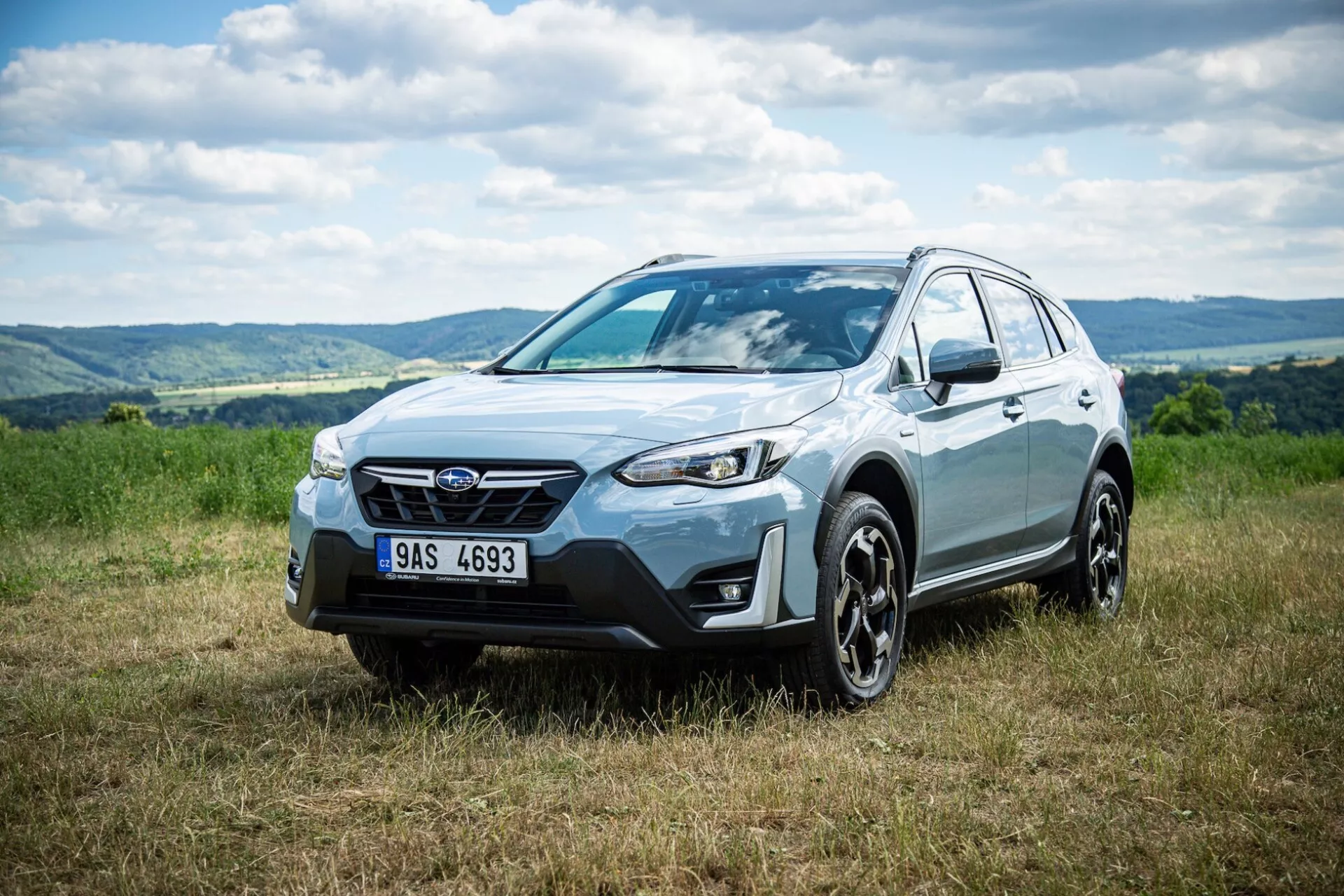 Crossover SUV Subaru XV 2021 zaparkowany na trawie z pagórkowatym tłem, podkreślający przednią fasadę, boczny profil i design koła