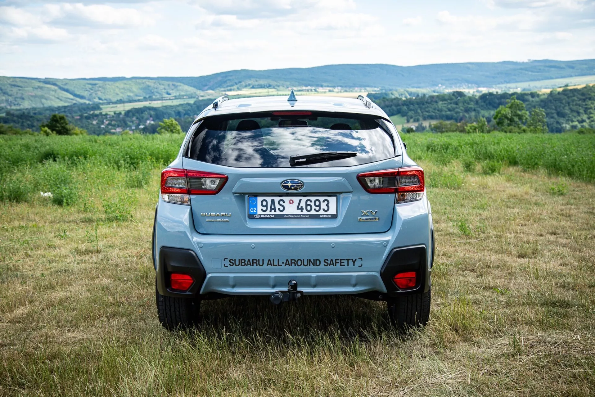 Tylny kąt Subaru XV 2021 na zewnątrz na polu z pagórkowatym tłem, podkreślający funkcje bezpieczeństwa i nowoczesne elementy projektowania SUV, takie jak tylny spoiler i śmiałe tylne światła