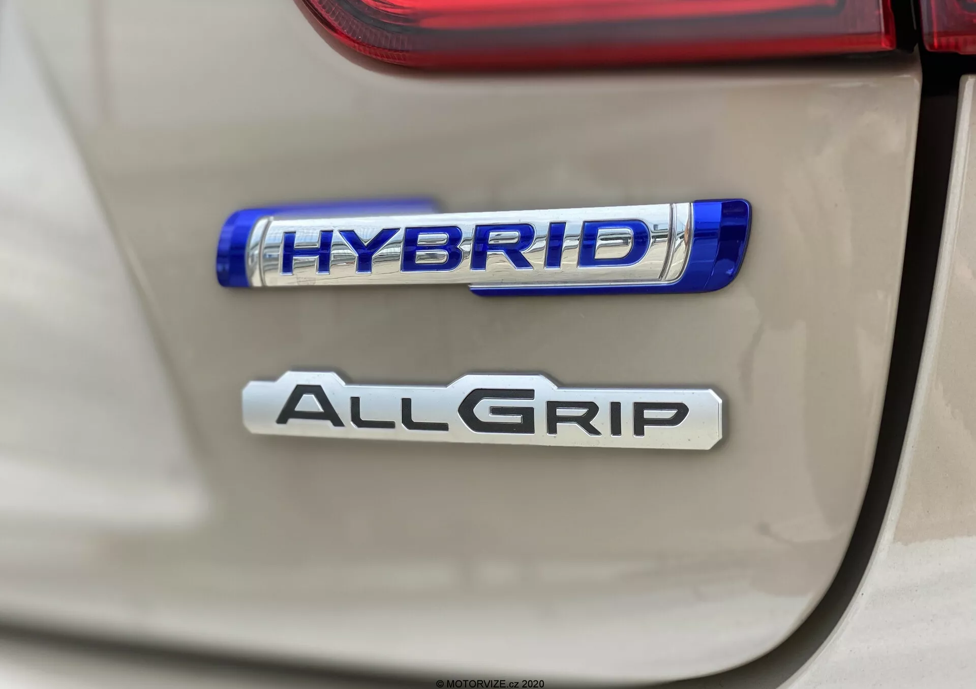 Zbliżenie tylnych emblematów Suzuki Ignis 2020, podkreślające funkcje 'HYBRID' i 'ALLGRIP'; wyraźne, bezpośrednie ujęcie z małą głębią ostrości, podkreślające ekologiczną technologię hybrydową i zaawansowany system napędu na wszystkie koła; naturalne oświetlenie z ostrymi szczegółami i lekkimi refleksami.