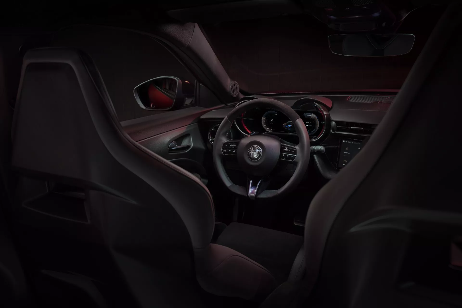Wnętrze Alfa-Romeo Junior (966) 2024 z sportowymi siedzeniami z materiału skóropodobnego i siateczki, wielofunkcyjną kierownicą pokrytą skórą oraz kokpitem zorientowanym na kierowcę z czerwonym oświetleniem akcentującym