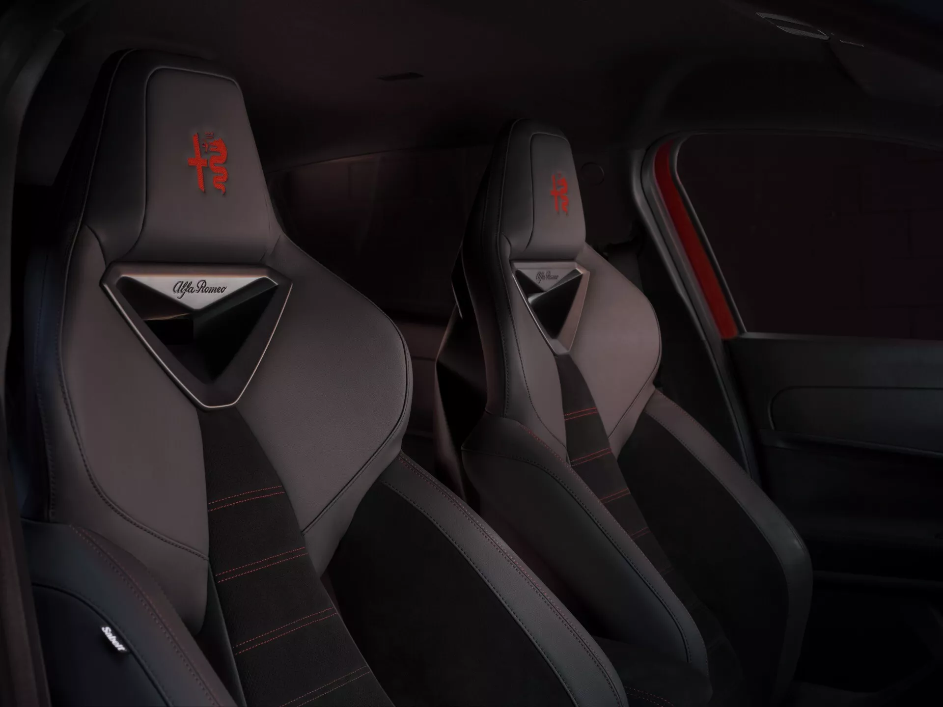 Widok wnętrza Alfa-Romeo Junior 2024 skupiający się na sportowych przednich fotelach z czerwonymi szwami i logo, prezentujący tapicerkę wysokiej jakości i sportowe detale designu