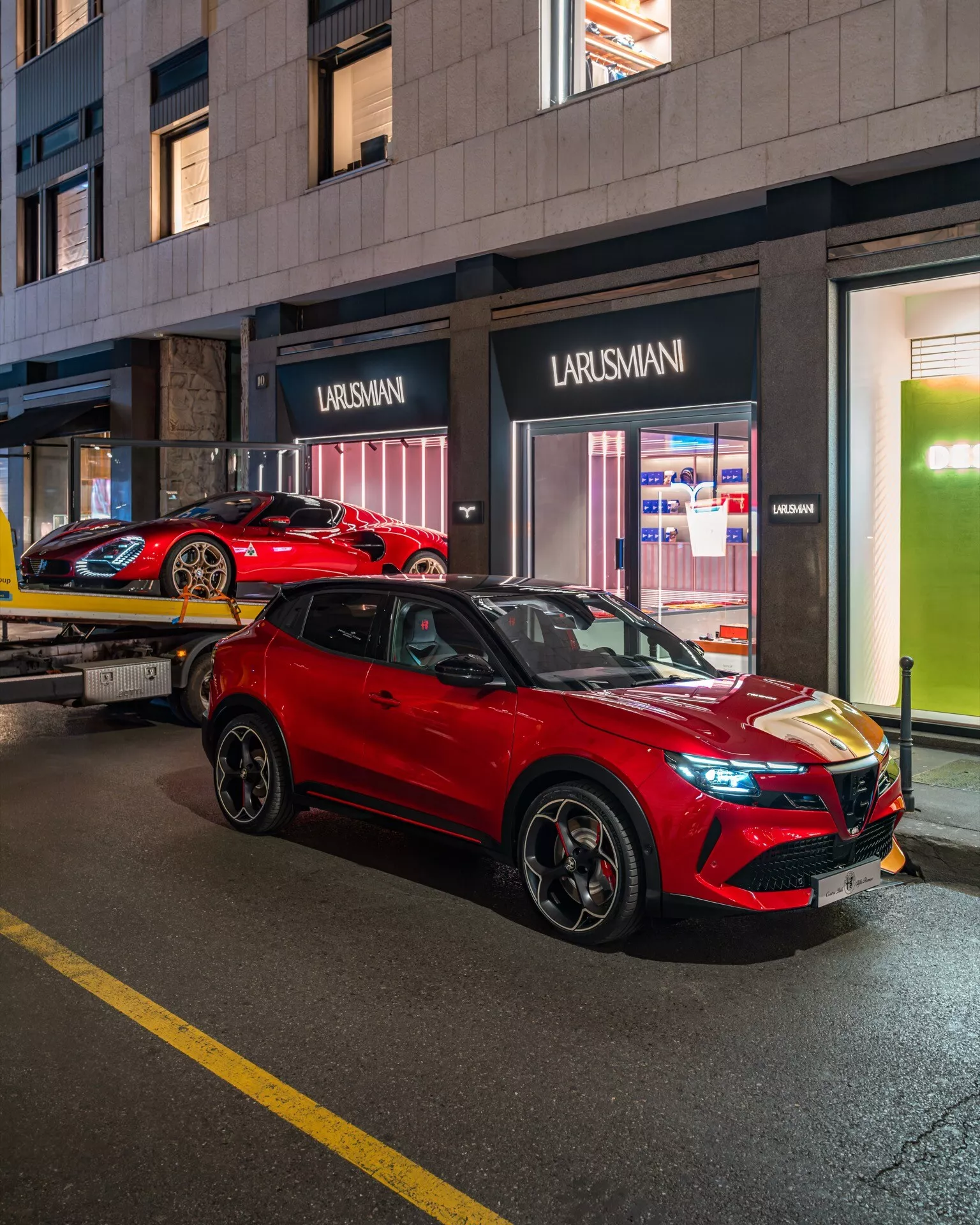 Jaskrawoczerwony SUV Alfa Romeo Junior 2024 zaparkowany na oświetlonej ulicy miasta w nocy, pokazujący elegancki design, reflektory LED i felgi ze stopu z perspektywy przedniej z trzech czwartych