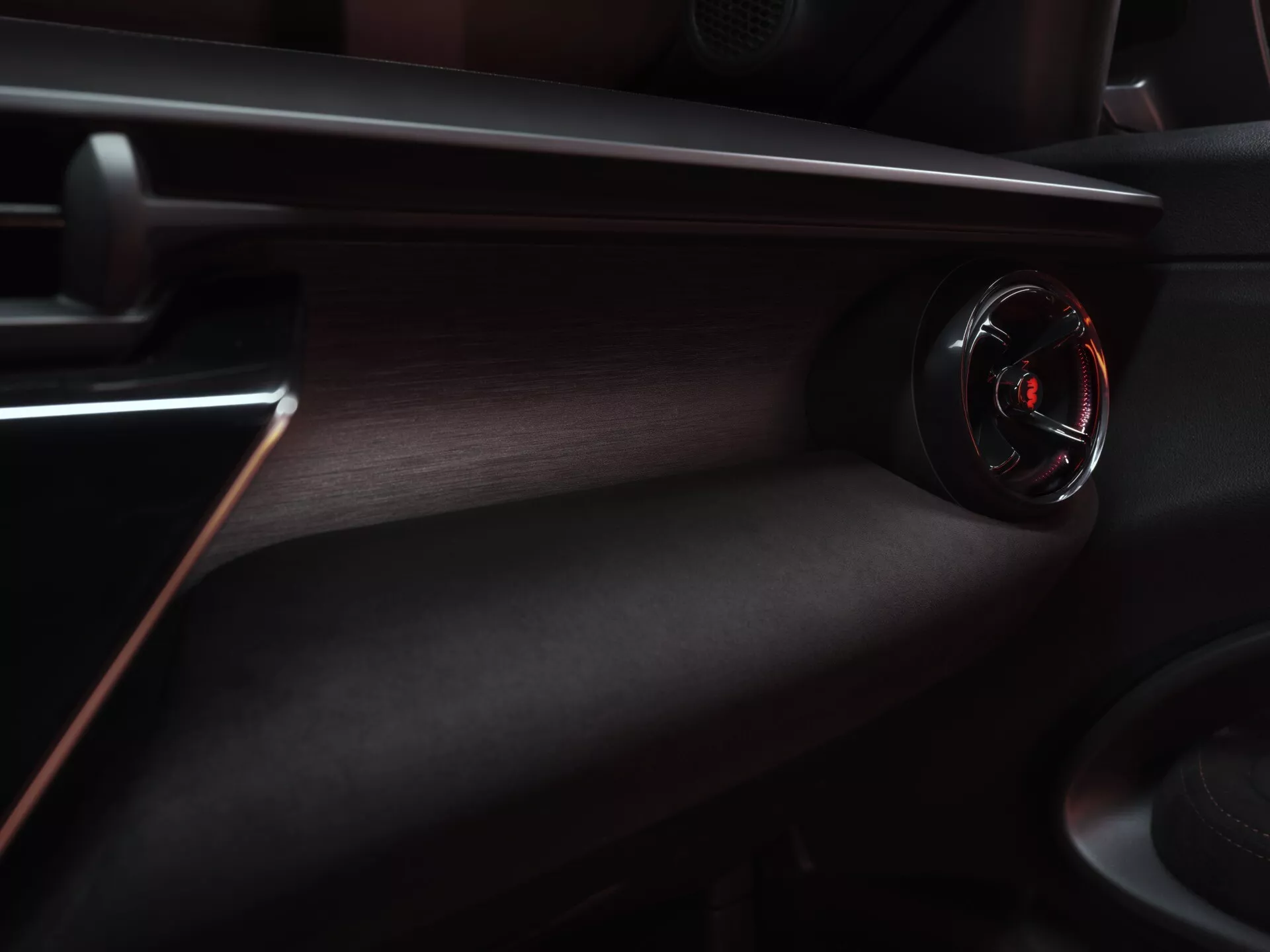 Widok wnętrza Alfa Romeo Junior 2024, podkreślający deska rozdzielcza po stronie pasażera z okrągłym nawiewem powietrza o błyszczącym czarnym wykończeniu i czerwonym akcencie, otoczona luksusową, ciemną, teksturowaną deską rozdzielczą z czerwonymi akcentami szwów