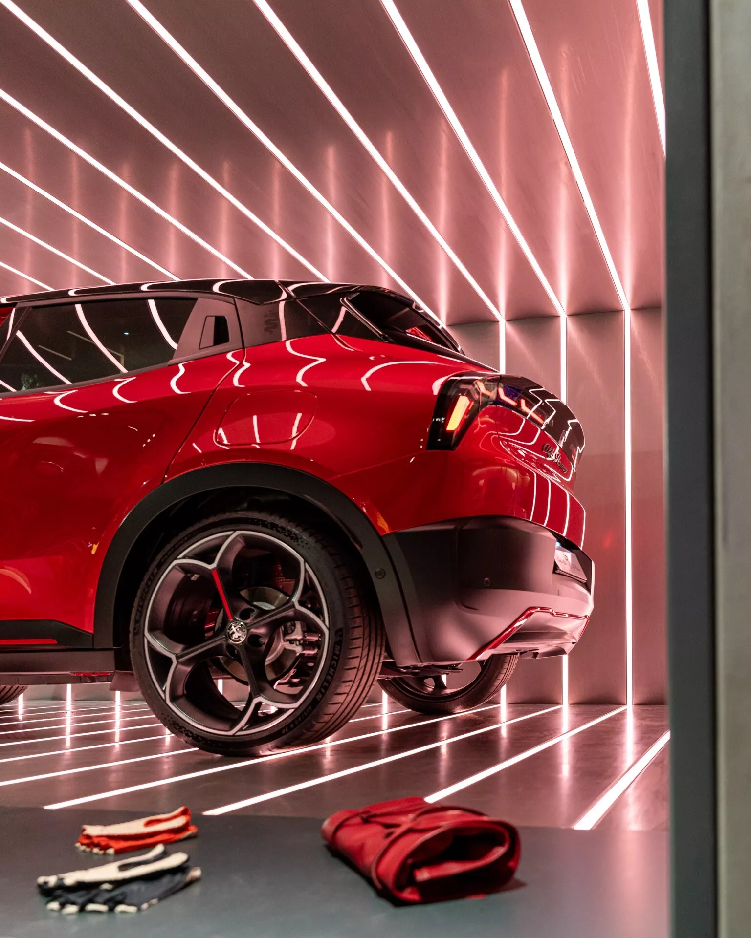 Zbliżenie na przednią część czerwonego Alfa Romeo Junior 2024, podkreślające zaawansowany system świateł, sportowy wzór kół i odblaskową powłokę lakieru w środowisku salonu