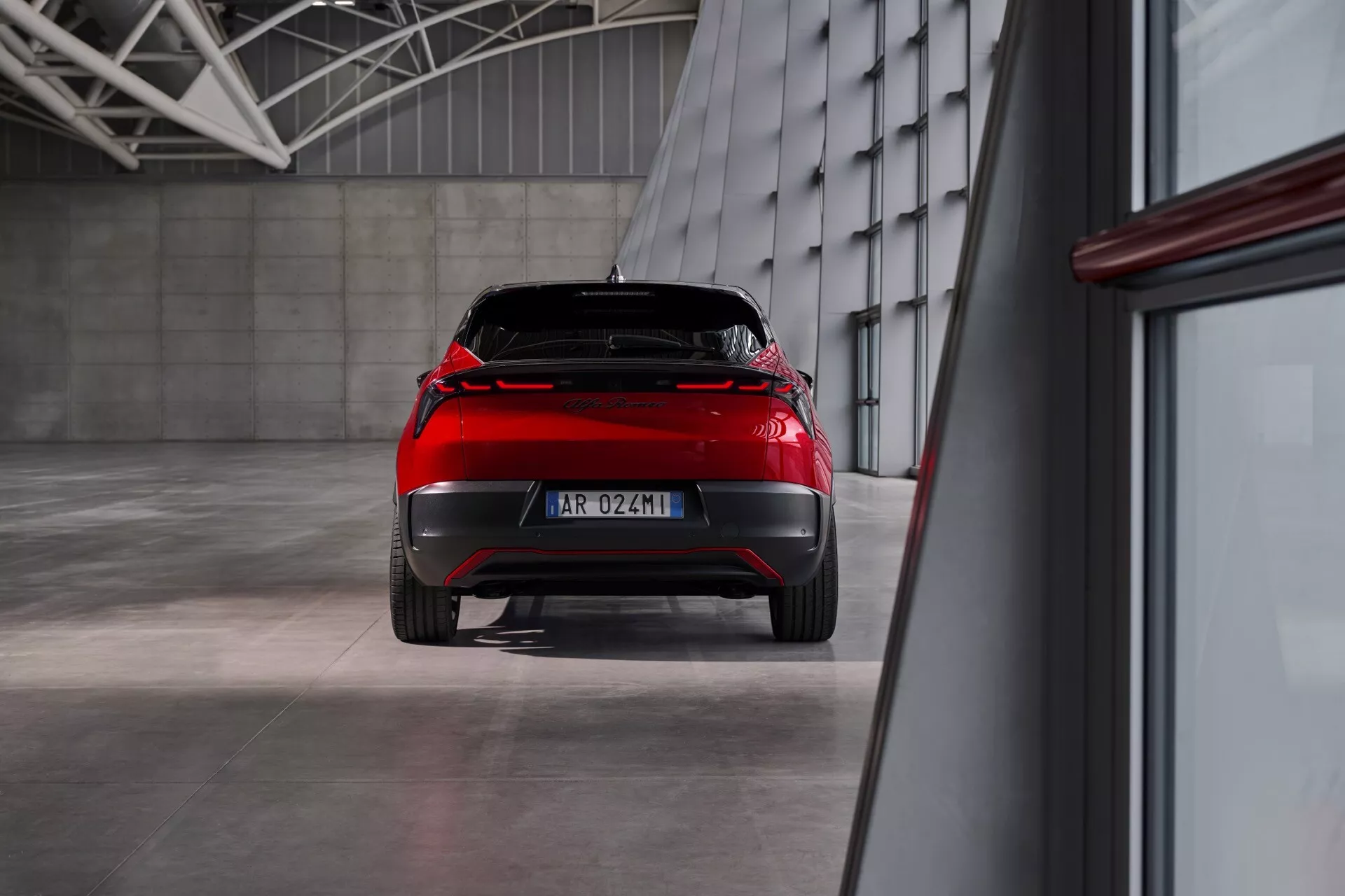 Tył Alfa Romeo Junior 2024 prezentujący cechy konstrukcyjne i diody LED w tylnej lampie w industrialnym otoczeniu z polerowaną podłogą i oświetleniem ambientalnym