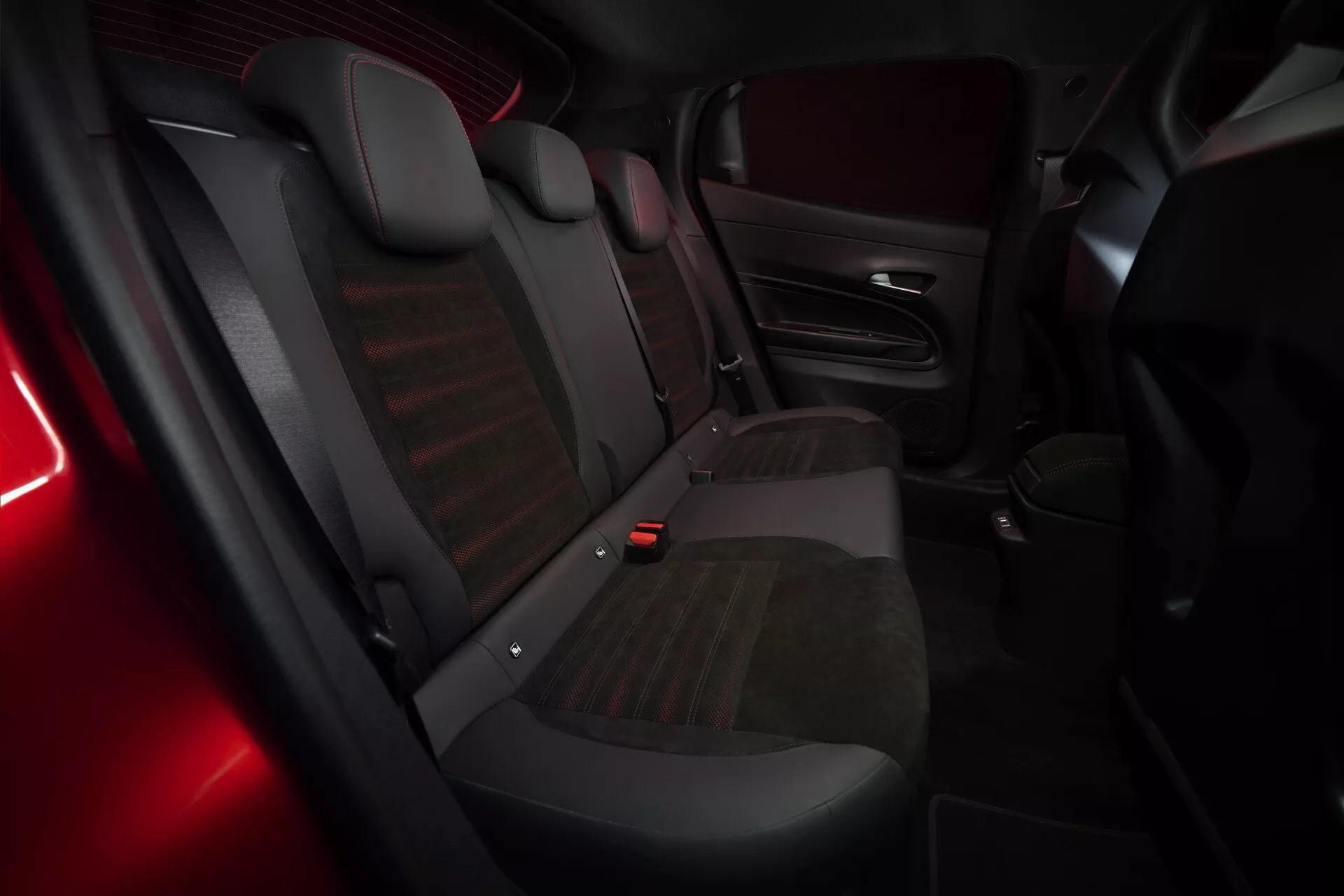 Widok wnętrza Alfa Romeo Junior (966) z 2024 roku z akcentem na tylną część pasażerską z trzema siedzeniami, mieszanej tapicerce i subtelne czerwone oświetlenie ambientowe