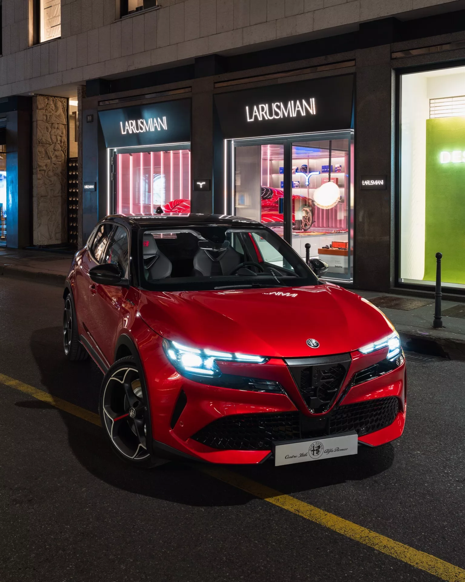 Czerwony sportowy pojazd użytkowy Alfa-Romeo Junior 2024 zaparkowany na miejskiej ulicy nocą, prezentujący sportowy i agresywny design z charakterystyczną kratą, nowoczesnymi reflektorami LED i kołami ze stopów lekkich o orientacji na wydajność