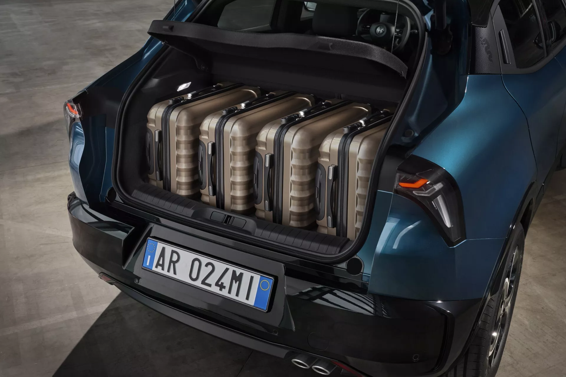 Alfa-Romeo Junior 966 z 2024 roku prezentuje swój przestronny niebieski bagażnik z wysokiego punktu widzenia, pokazując układ bagażu i cechy konstrukcyjne, w tym kształt świateł tylnych i krzywiznę zderzaka tylnego.