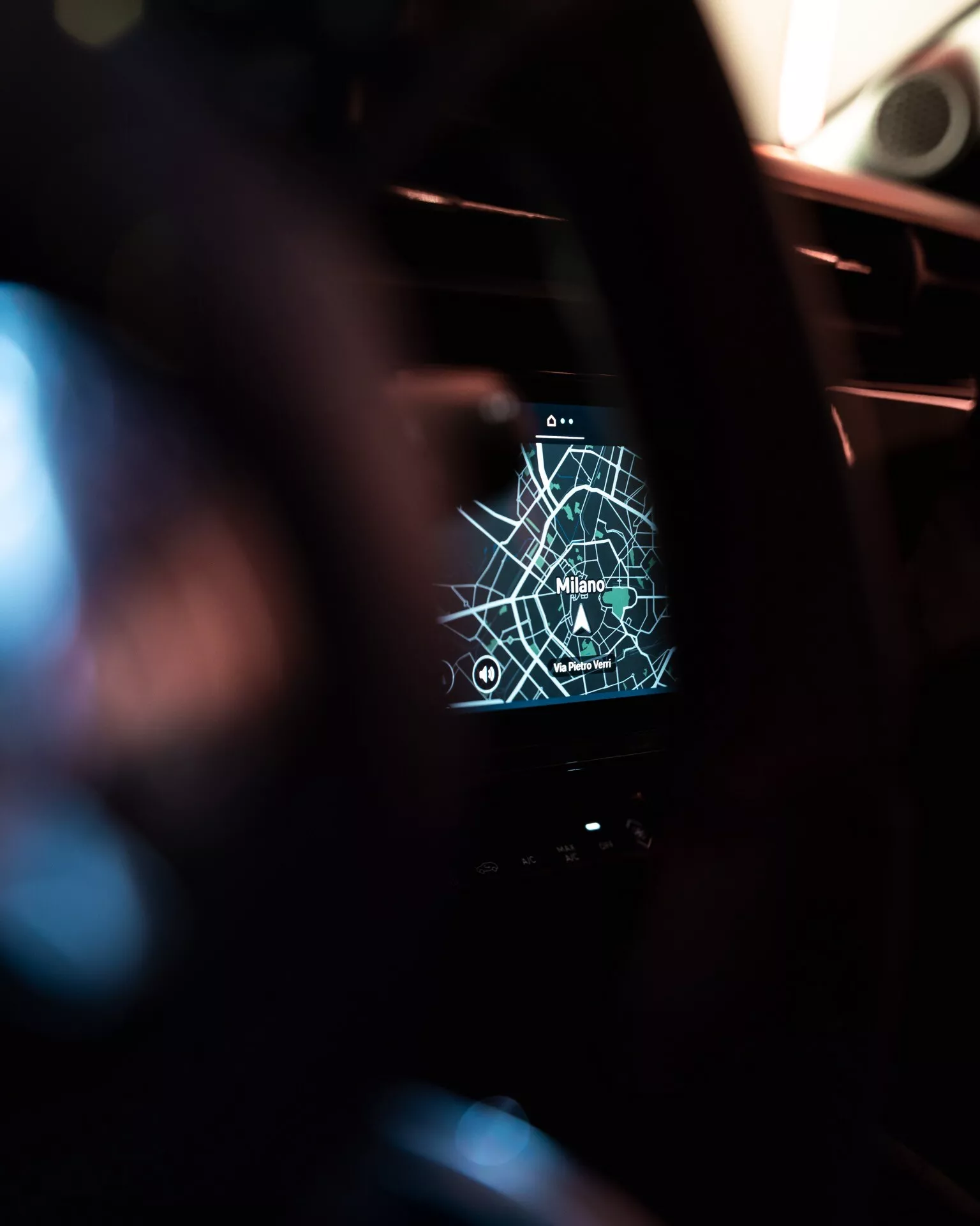 Widok wnętrza Alfa Romeo Junior 2024 skupiony na systemie infotainment pokazującym mapę GPS Mediolanu z ikonami nawigacyjnymi, wykonany z perspektywy kierowcy z niewielką głębią ostrości