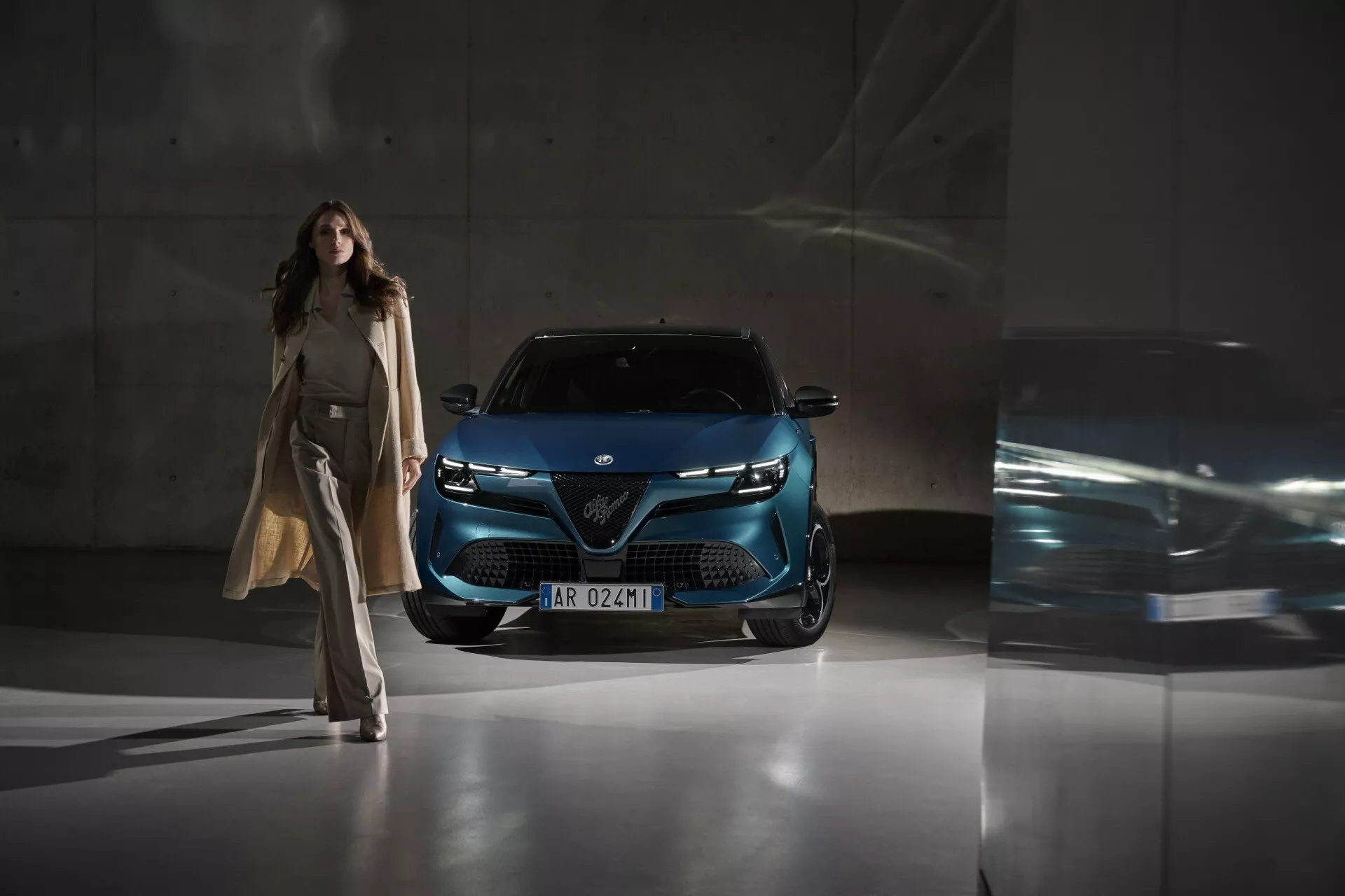 Alfa-Romeo Junior 2024 sfotografowany pod niskim kątem przednim, pokazujący grill, reflektory LED i nowoczesny przód w głębokim metalicznym niebieskim, podkreślając zaawansowaną technologię oświetleniową i design w miejskim otoczeniu