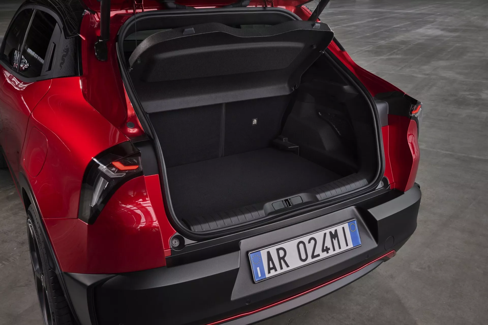 Tylny widok czerwonego Alfa-Romeo Junior 966 z 2024 roku prezentujący pojemność bagażnika i nowoczesne elementy designu takie jak automatyczna klapa bagażnika, czarny wstawka zderzaka dla ochrony przed zadrapaniami i technologii parkowania oraz stylowe tylne światła LED.