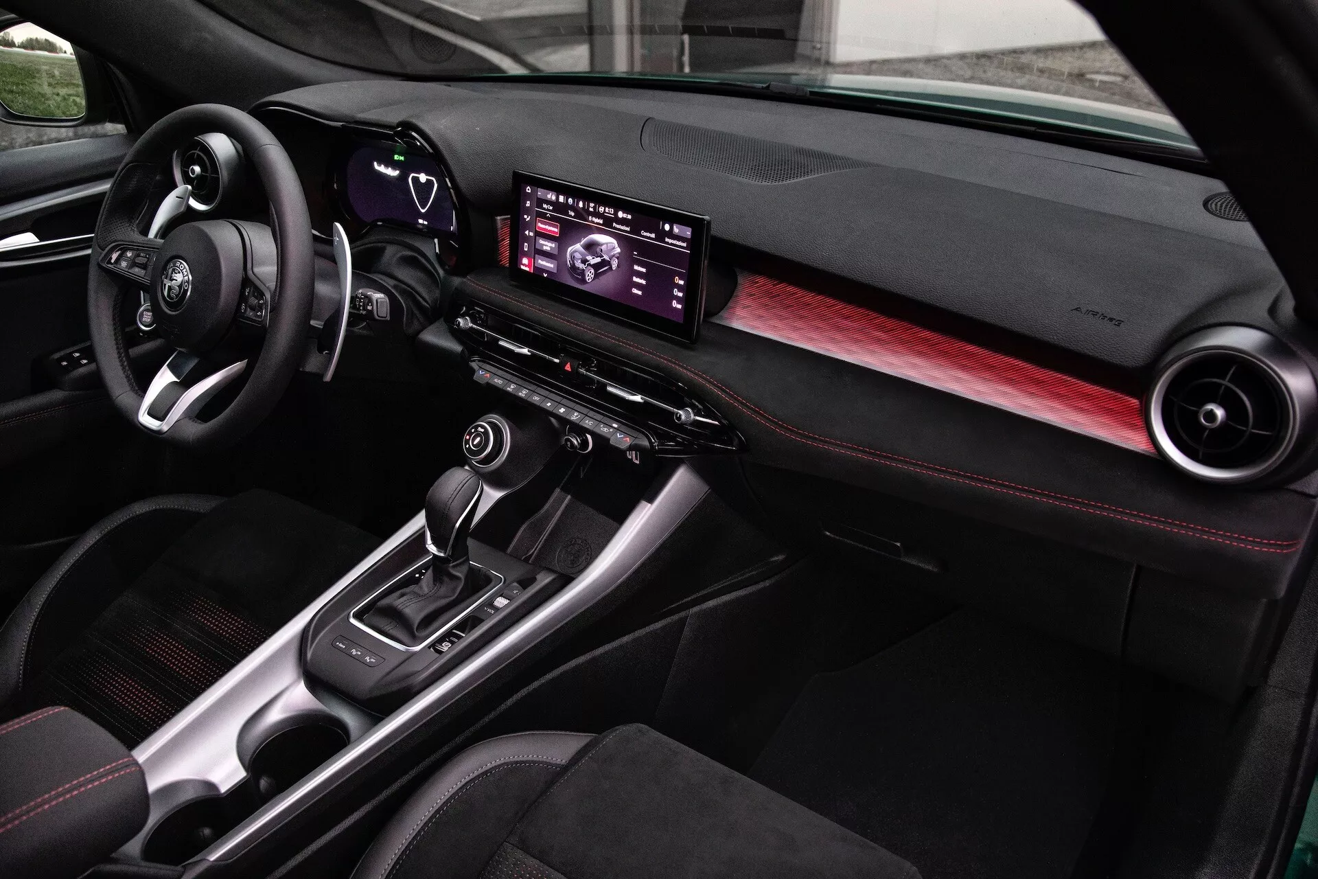 Wnętrze Alfa Romeo Tonale 2022 z nowoczesną deską rozdzielczą, cyfrowym centrum infotainment, akcentami z włókna węglowego i siedzeniami z czerwonymi szwami, widok z perspektywy pasażera przedniego