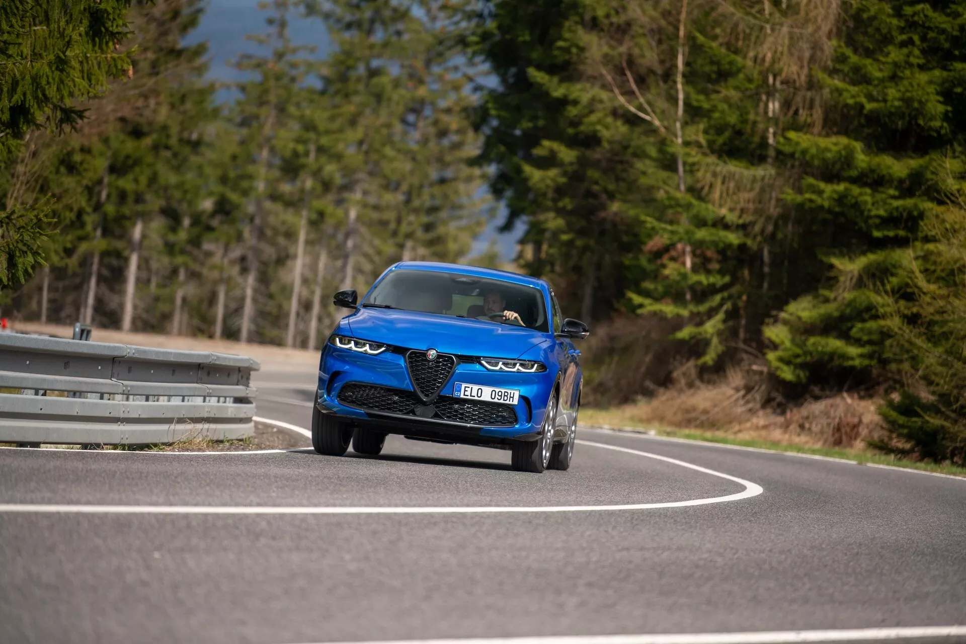 Alfa-Romeo Tonale 2022 w ruchu na krętej drodze, prezentujące dynamiczny design, reflektory LED, wloty powietrza, sportowy styl kabrioletu i luksusowe cechy z niskiej perspektywy trzy czwarte z przodu
