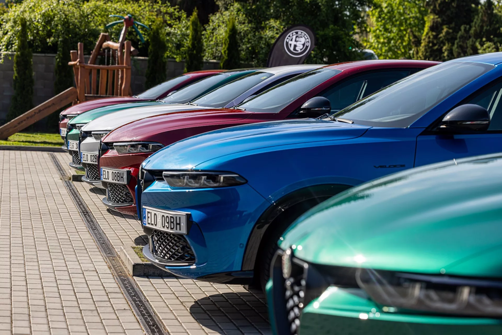 Linia Alfa-Romeo Tonale 2022 w żywych kolorach prezentująca luksusowy design z zaawansowanymi reflektorami LED, zaparkowana w ułożeniu diagonalnym skupiającym się na lewej przedniej stronie z niskiego na średni kąt wysokości na utwardzonej powierzchni obok trawnika, możliwie w salonie dealerskim lub na wydarzeniu miłośników samochodów