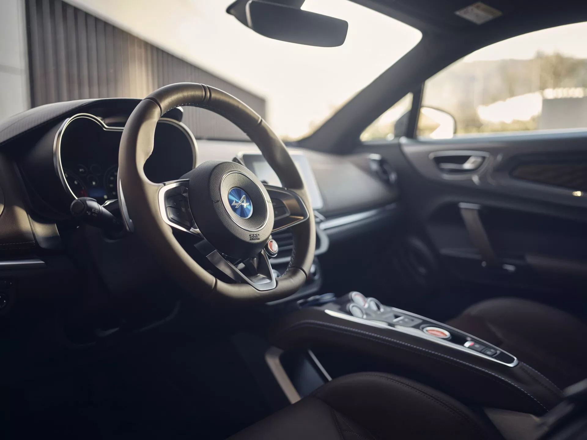 Wnętrze Alpine A110 2017 ukazujące obszar kokpitu kierowcy, zawierające wielofunkcyjną kierownicę z emblematem, cyfrowy kokpit, centralną konsolę z pokrętłem do systemu infotainment oraz luksusowe skórzane siedzenia