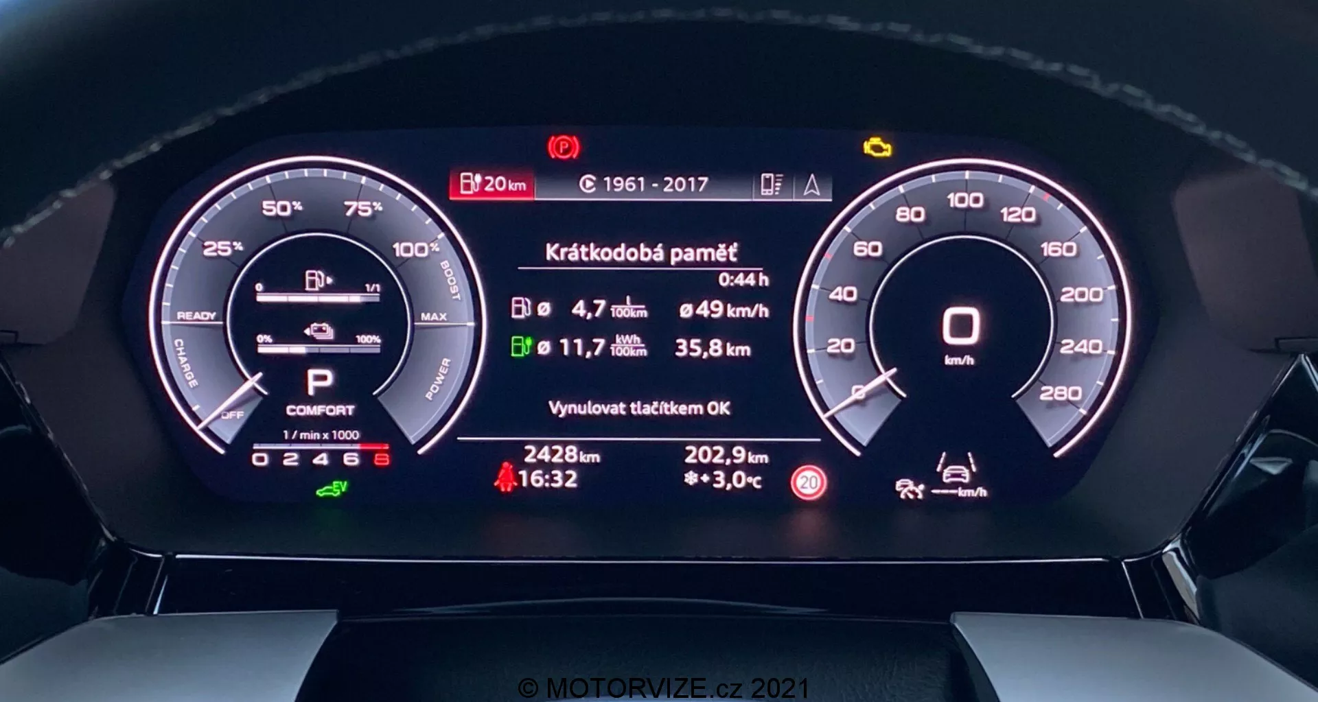 Zbliżenie na cyfrowy zestaw wskaźników Audi A3 2020 Sportback z perspektywy kierowcy. Widok z przodu pokazuje szczegółowe wyświetlacz cyfrowe obrotomierza, wskaźnika baterii, wybór biegów, tryb jazdy, średnią prędkość, zużycie paliwa, dystans do opróżnienia zbiornika, temperaturę zewnętrzną oraz komunikat o ostatnim przeglądzie. Nowoczesny design łączy cyfrowe i analogowe elementy, zapewniając zaawansowane technologicznie i intuicyjne wrażenia.
