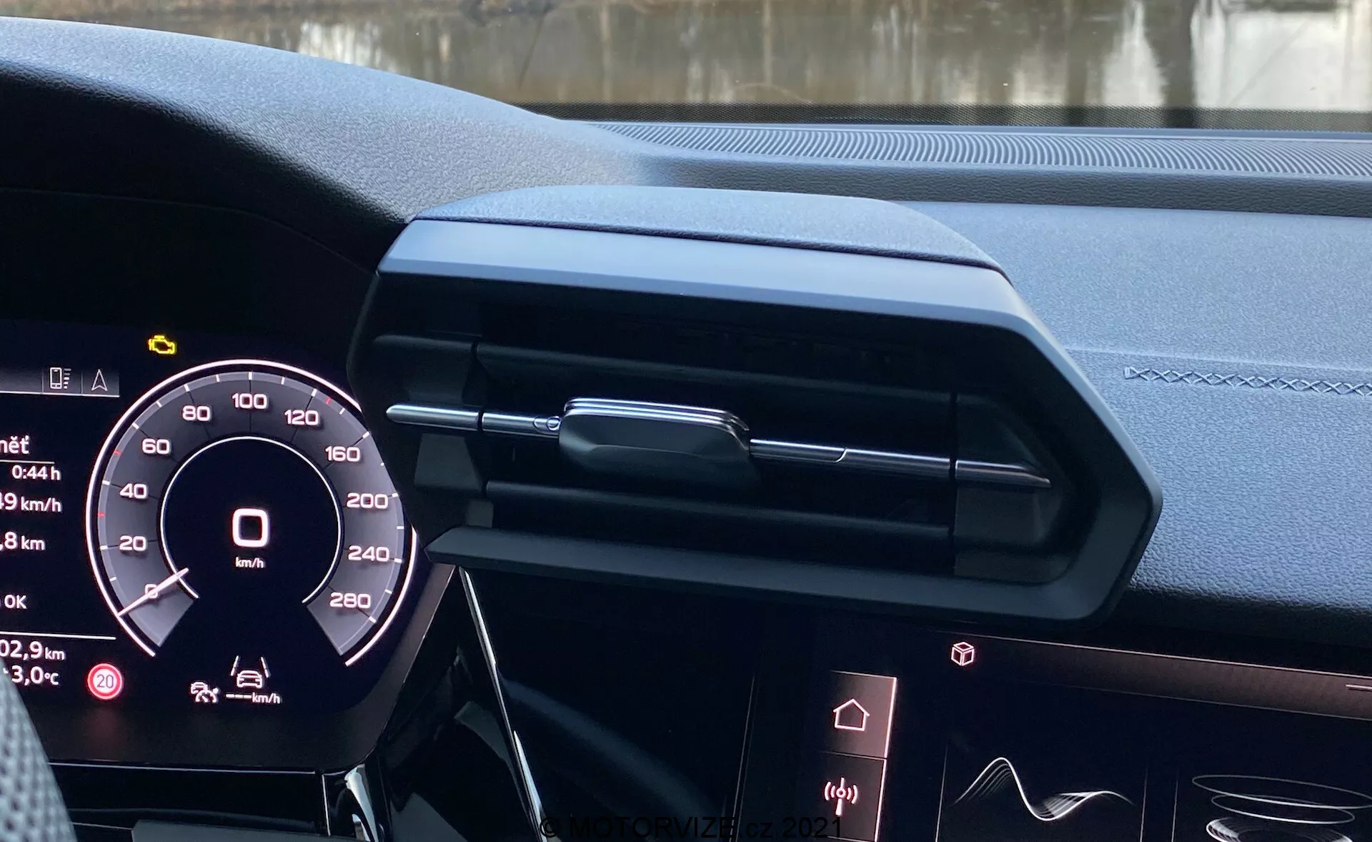 Widok wnętrza Audi A3 Sportback 2020 z siedzenia kierowcy, pokazujący cyfrowy zestaw wskaźników, elegancki design deski rozdzielczej z zamkniętym centralnym otworem wentylacyjnym i ozdobnym wykończeniem, krawędź ekranu infotainmentowego, wysokiej jakości materiały skórzane z przeszyciami, oświetlenie ambientowe i częściowo widoczną kierownicę z możliwymi przyciskami sterującymi, podkreślający nowoczesną technologię samochodową i luksusowy design.
