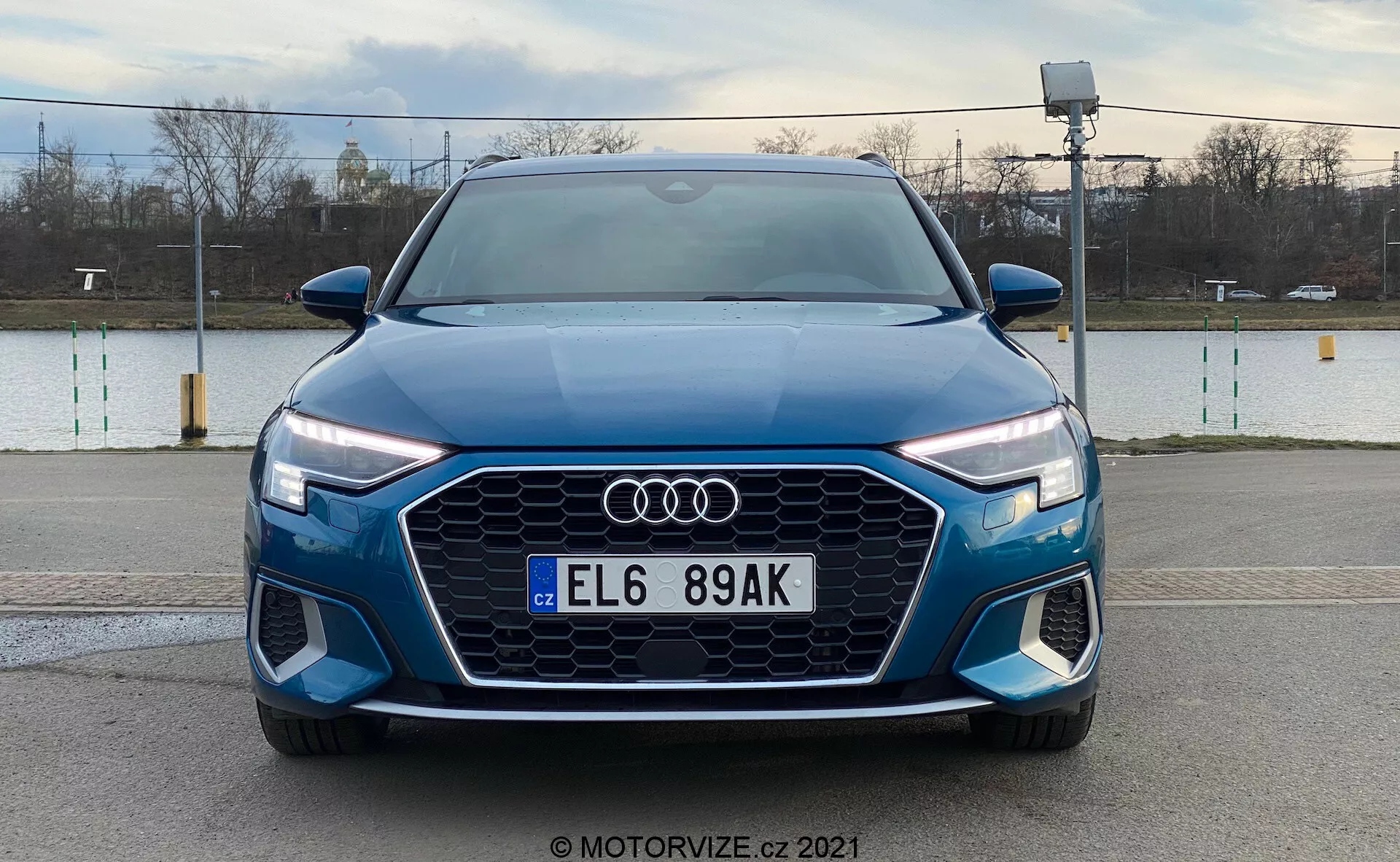 Widok z przodu niebieskiego Audi A3 Sportback 2020 prezentujący jego wyraźny grill Singleframe z heksagonalnym wzorem, centralnie umieszczone logo Audi, reflektory LED ze światłami do jazdy dziennej oraz przedni zderzak z dodatkowymi wlotami powietrza i prawdopodobnymi światłami przeciwmgielnymi, na tle zewnętrznym.