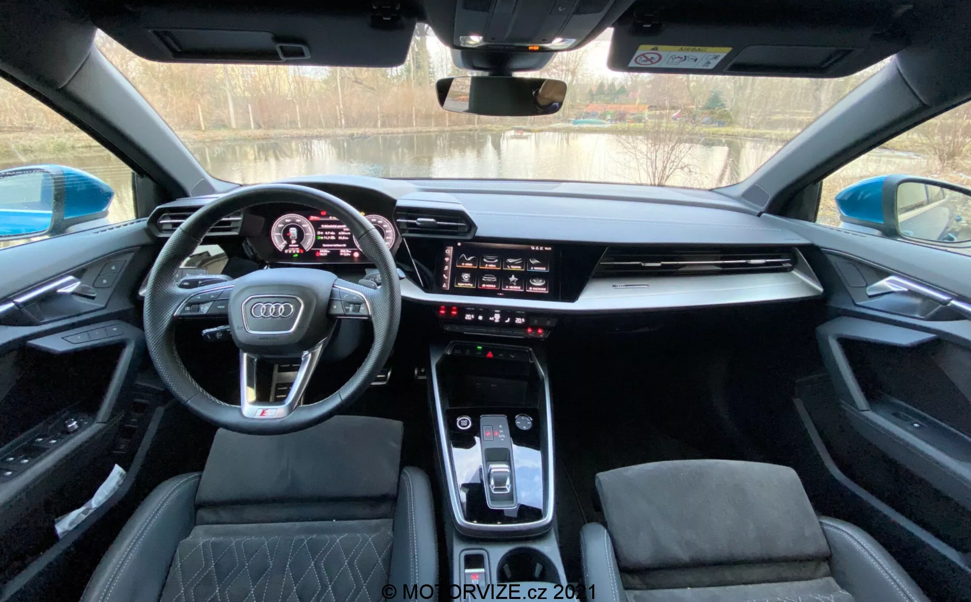 Wnętrze Audi A3 Sportback 2020 z perspektywy kierowcy, ukazujące nowoczesną deskę rozdzielczą z cyfrowym panelem przyrządów, sportową wielofunkcyjną kierownicą z logo Audi, zintegrowanym ekranem dotykowym systemu infotainment, elegancką konsolę środkową z automatycznym selektorem biegu, sterowaniem klimatyzacją i sportowymi siedzeniami z diamentowymi przeszyciami pod panoramicznym dachem.